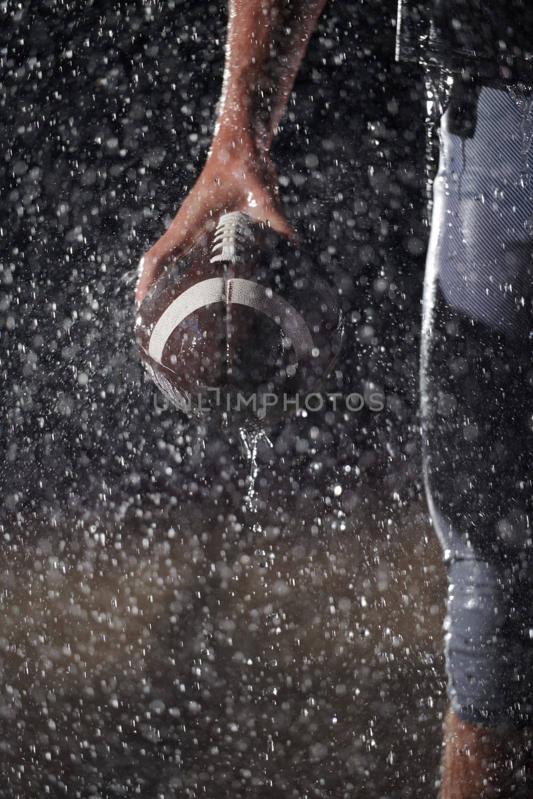 Close up of American Football Athlete Warrior Standing on a Field focus on his Helmet and Ready to Play. Player Preparing to Run, Attack and Score Touchdown. Rainy Night with Dramatic lens flare by dotshock