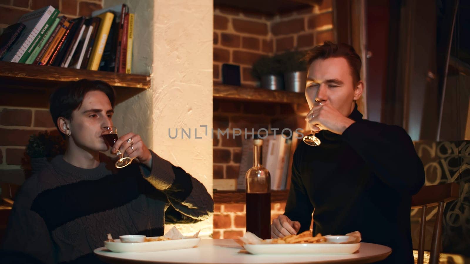 Two friends are sitting in restaurant, chatting and drinking alcoholic drink. Media. Two young men are drinking alcoholic tincture in restaurant. Cozy meeting of two friends in restaurant with alcoholic drink.