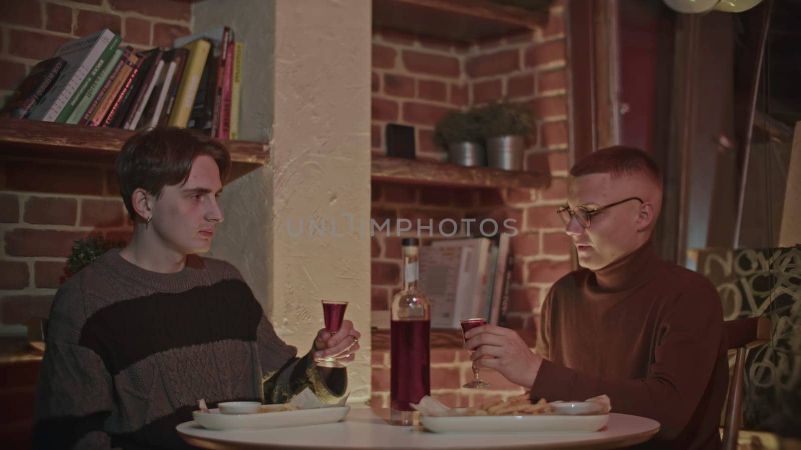 Two young male friends spend time together at restaurant or bar. Media. Men drinking alcohol