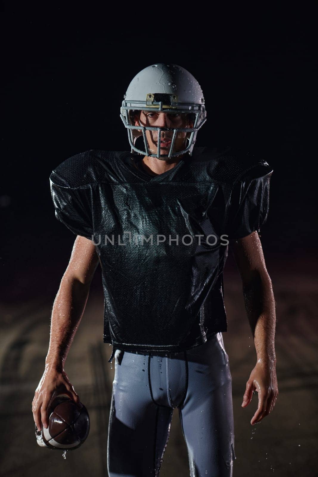 American Football Field: Lonely Athlete Warrior Standing on a Field Holds his Helmet and Ready to Play. Player Preparing to Run, Attack and Score Touchdown. by dotshock