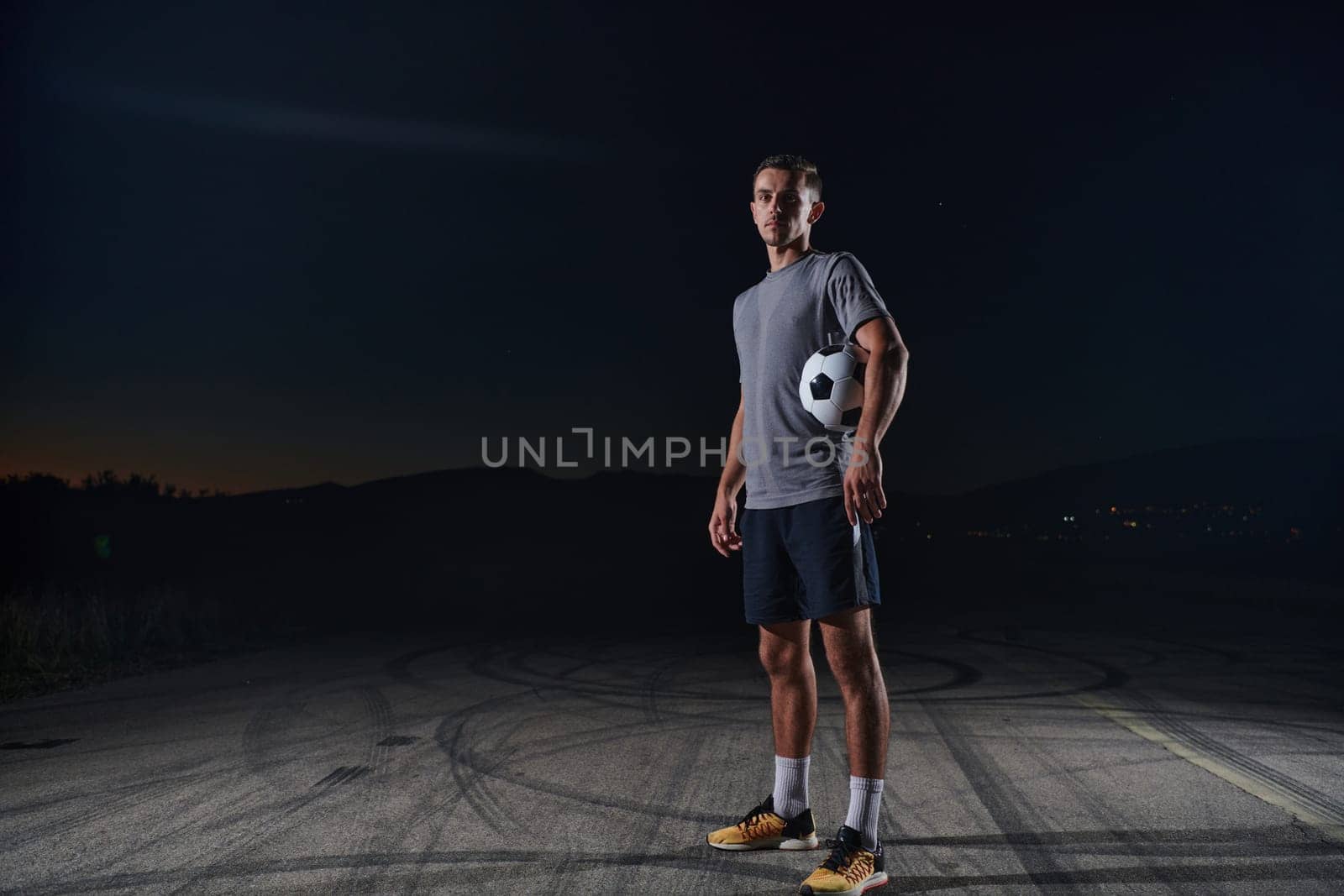 Portrait of a young handsome soccer player man on a street playing with a football ball. by dotshock