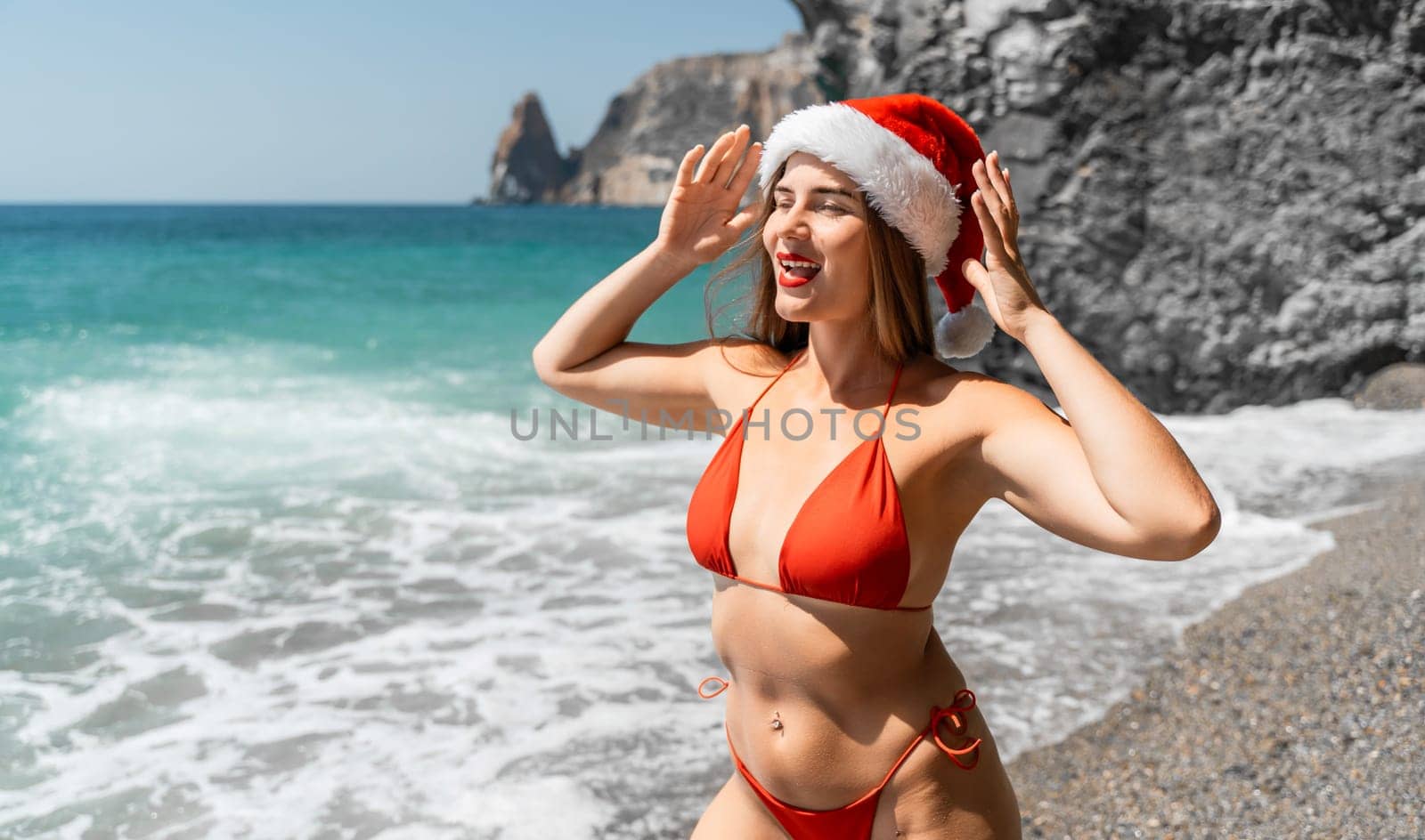 A woman in Santa hat on the seashore, dressed in a red swimsuit. New Year's celebration in a hot country.