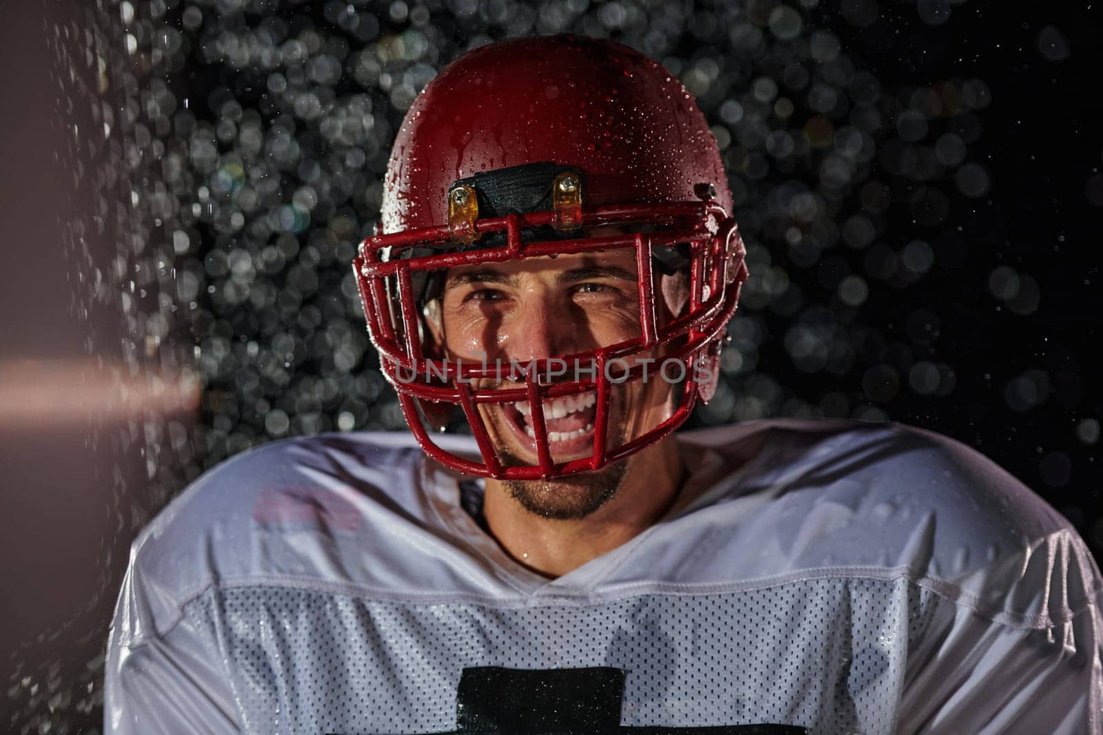 American Football Field: Lonely Athlete Warrior Standing on a Field Holds his Helmet and Ready to Play. Player Preparing to Run, Attack and Score Touchdown. Rainy Night with Dramatic Fog, Blue Light by dotshock