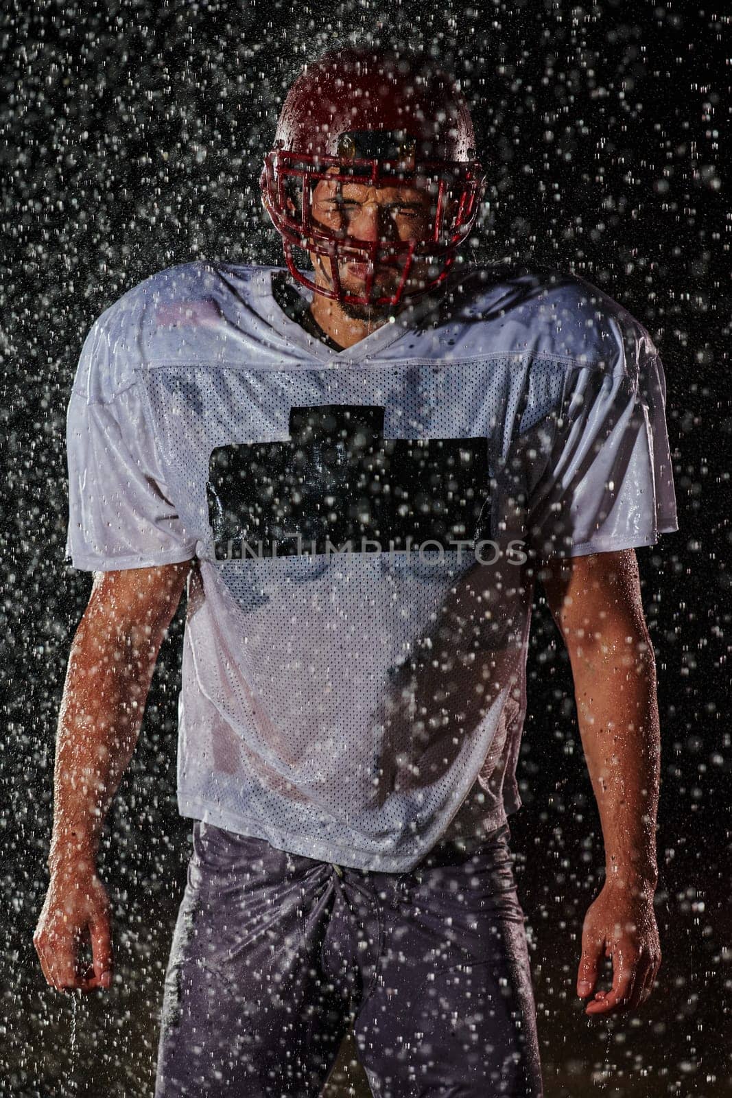 American Football Field: Lonely Athlete Warrior Standing on a Field Holds his Helmet and Ready to Play. Player Preparing to Run, Attack and Score Touchdown. Rainy Night with Dramatic Fog, Blue Light by dotshock