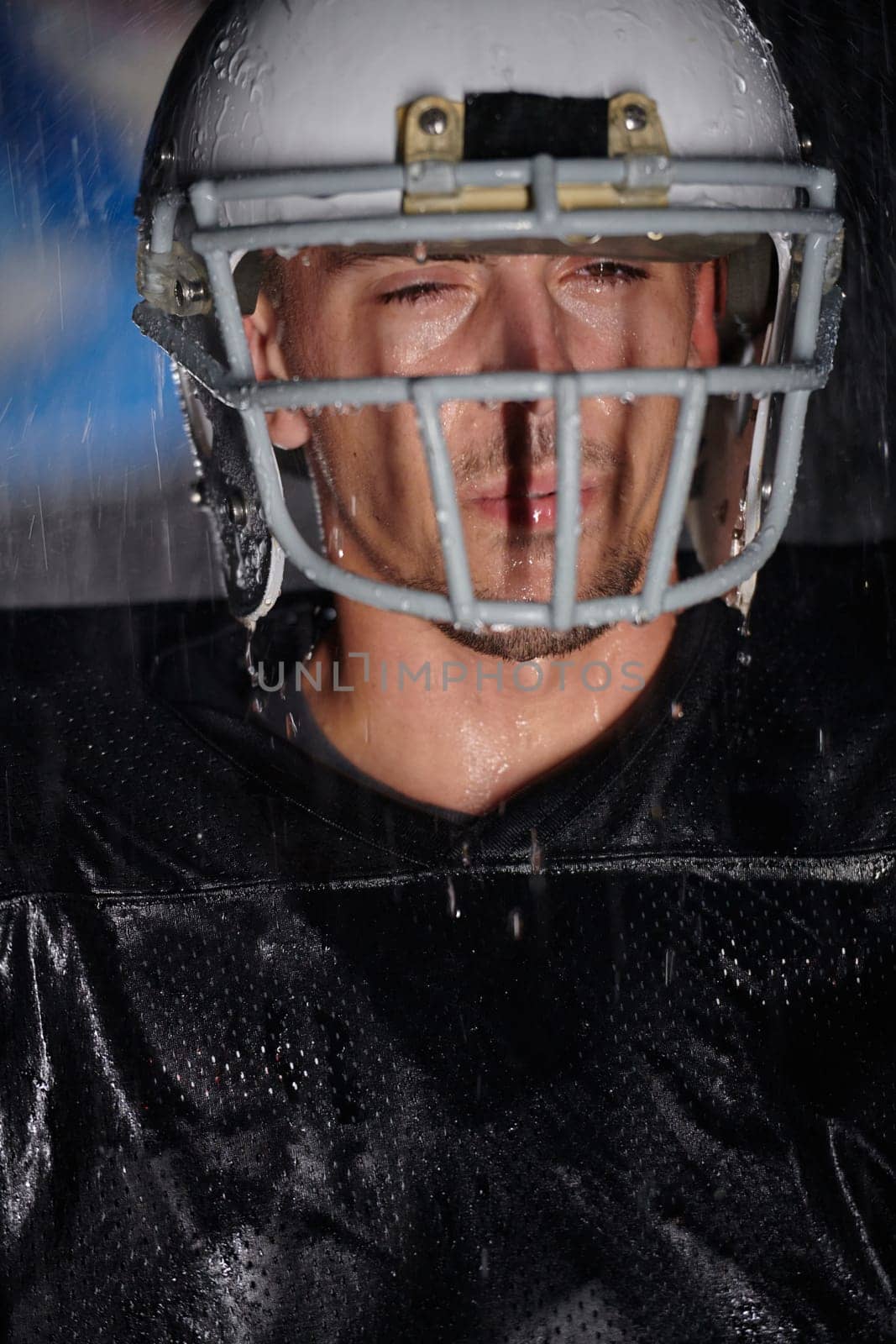 American Football Field: Lonely Athlete Warrior Standing on a Field Holds his Helmet and Ready to Play. Player Preparing to Run, Attack and Score Touchdown. Rainy Night with Dramatic Fog, Blue Light by dotshock