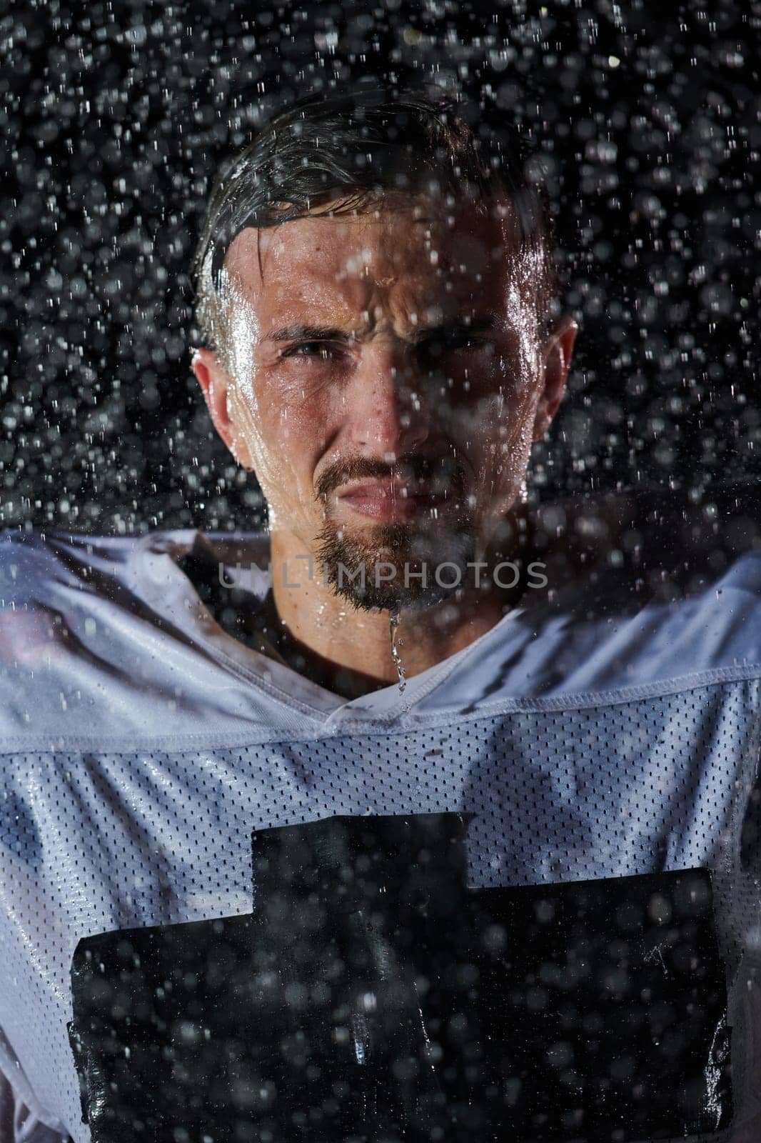 American Football Field: Lonely Athlete Warrior Standing on a Field Holds his Helmet and Ready to Play. Player Preparing to Run, Attack and Score Touchdown. Rainy Night with Dramatic Fog, Blue Light.