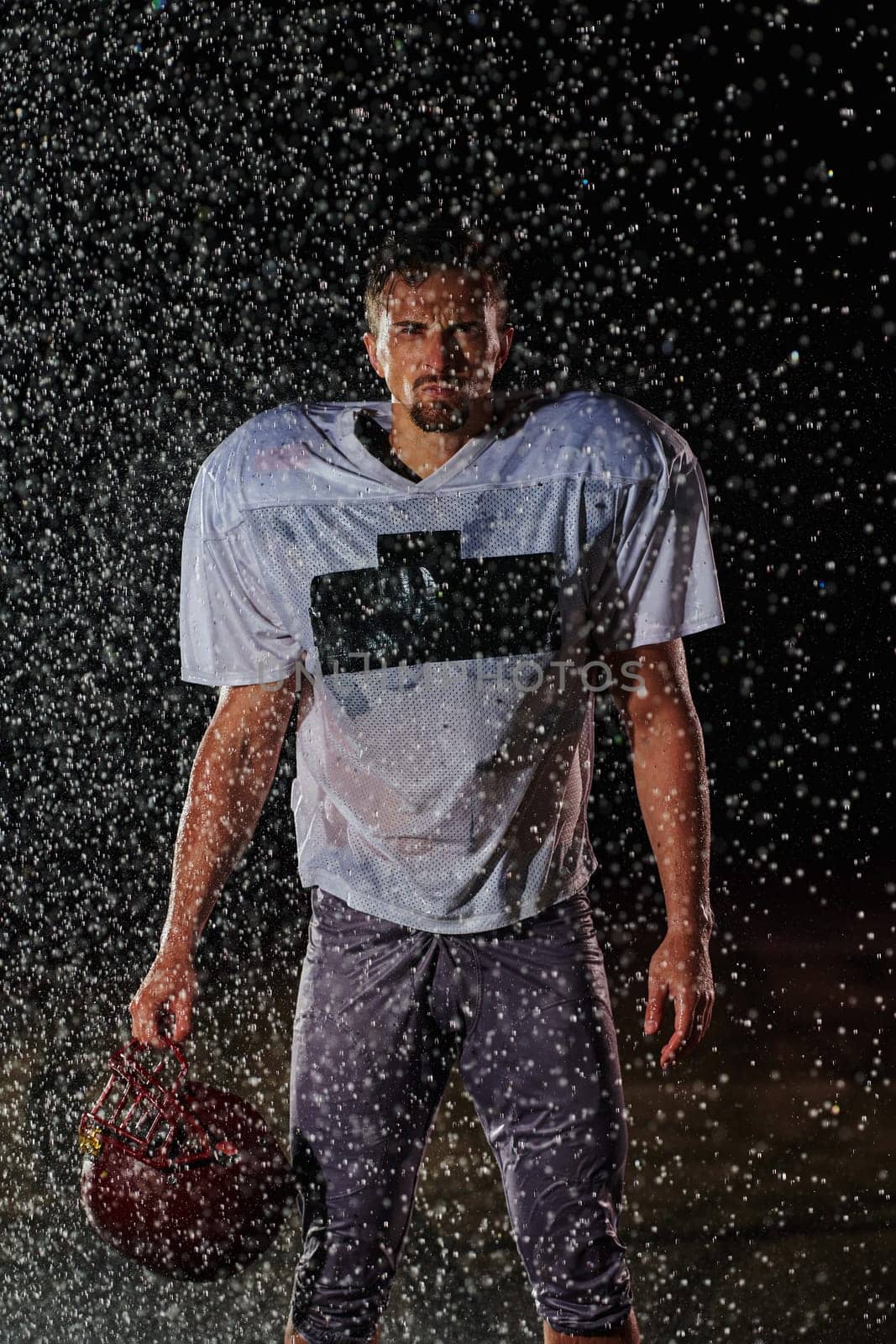 American Football Field: Lonely Athlete Warrior Standing on a Field Holds his Helmet and Ready to Play. Player Preparing to Run, Attack and Score Touchdown. Rainy Night with Dramatic Fog, Blue Light.