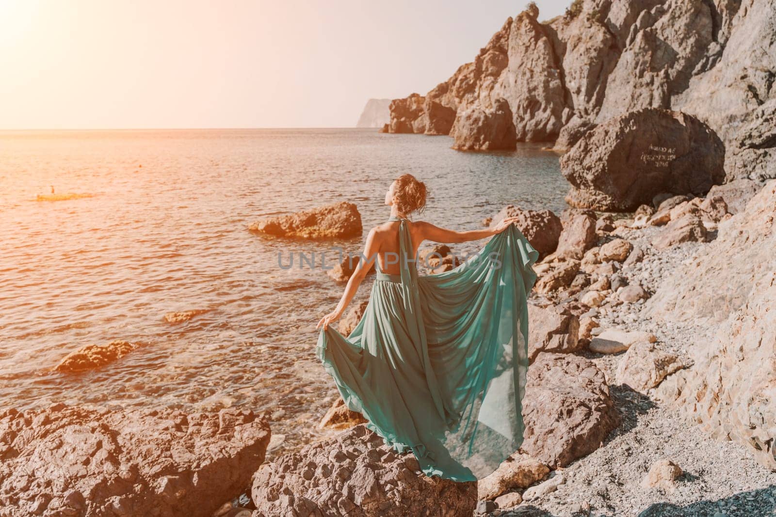 Woman green dress sea. Woman in a long mint dress posing on a beach with rocks on sunny day. Girl on the nature on blue sky background