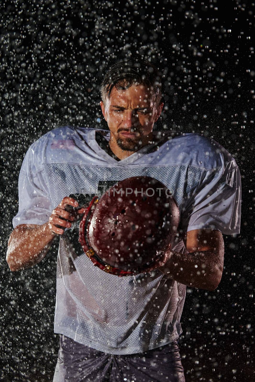 American Football Field: Lonely Athlete Warrior Standing on a Field Holds his Helmet and Ready to Play. Player Preparing to Run, Attack and Score Touchdown. Rainy Night with Dramatic Fog, Blue Light by dotshock