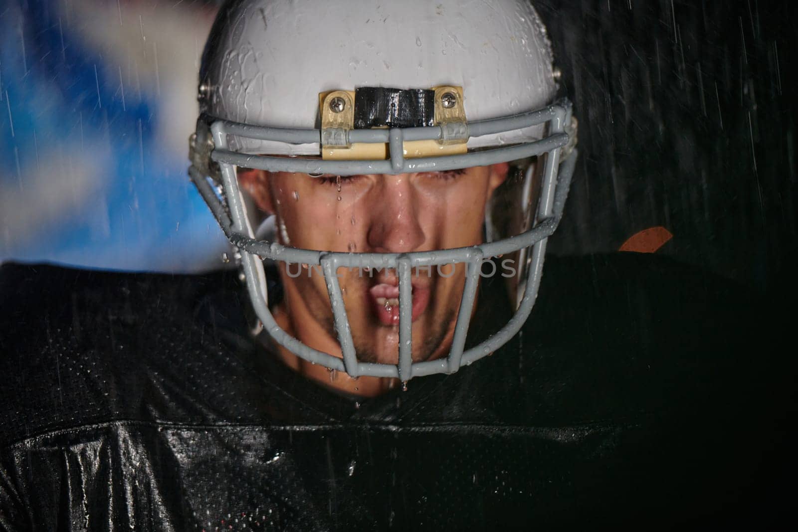 American Football Field: Lonely Athlete Warrior Standing on a Field Holds his Helmet and Ready to Play. Player Preparing to Run, Attack and Score Touchdown. Rainy Night with Dramatic Fog, Blue Light.