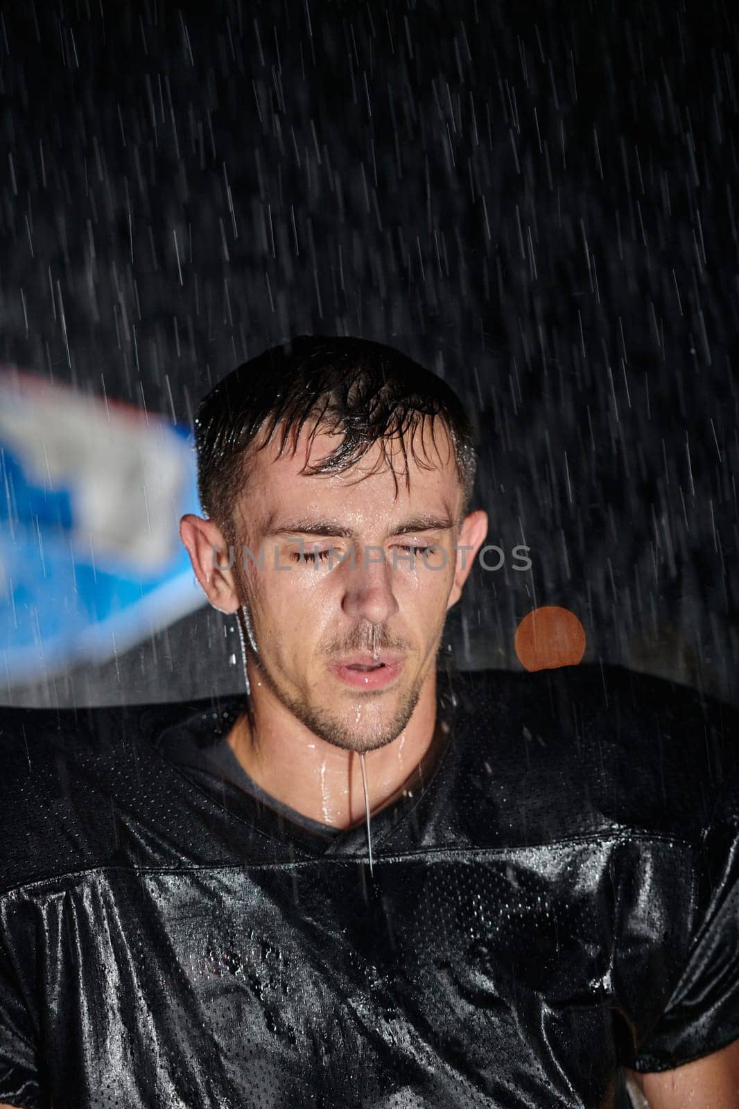 American Football Field: Lonely Athlete Warrior Standing on a Field Holds his Helmet and Ready to Play. Player Preparing to Run, Attack and Score Touchdown. Rainy Night with Dramatic Fog, Blue Light.