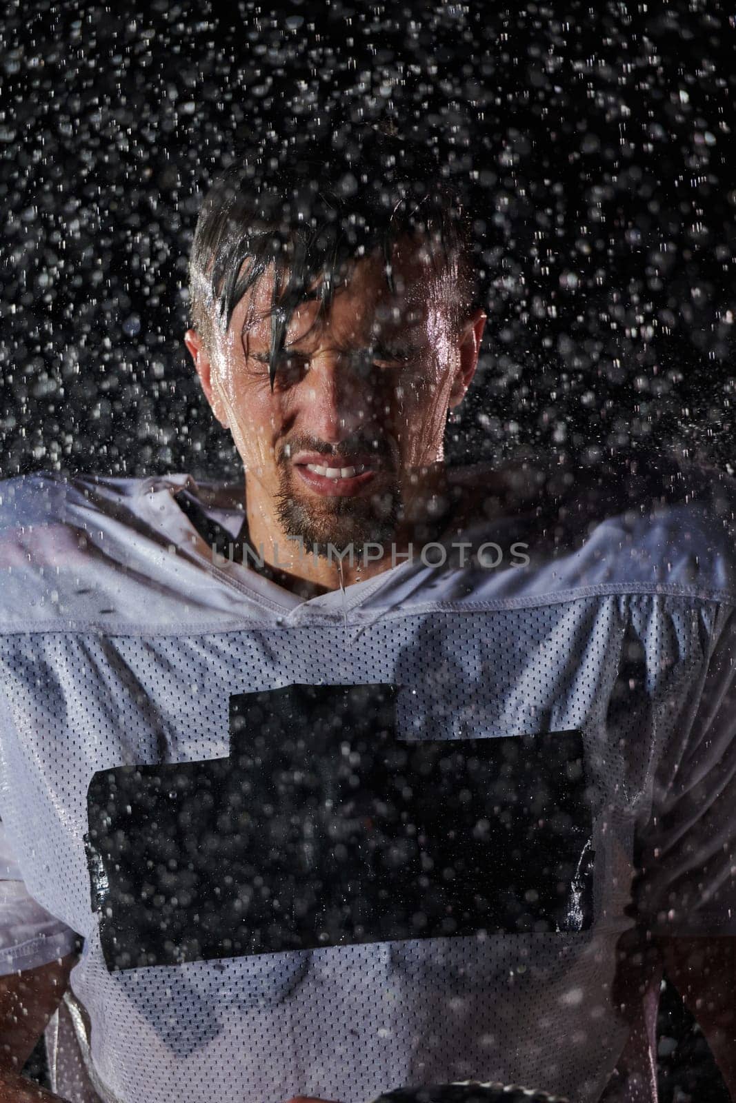 American Football Field: Lonely Athlete Warrior Standing on a Field Holds his Helmet and Ready to Play. Player Preparing to Run, Attack and Score Touchdown. Rainy Night with Dramatic Fog, Blue Light by dotshock