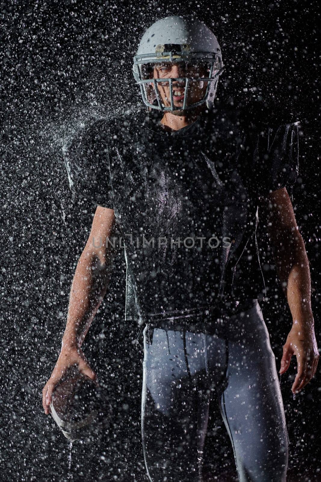 American Football Field: Lonely Athlete Warrior Standing on a Field Holds his Helmet and Ready to Play. Player Preparing to Run, Attack and Score Touchdown. Rainy Night with Dramatic Fog, Blue Light by dotshock