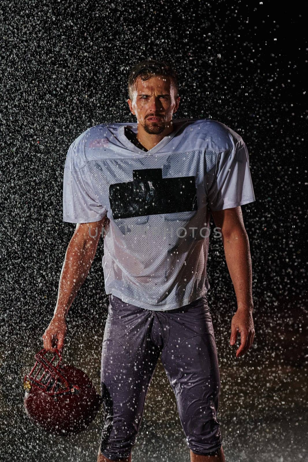 American Football Field: Lonely Athlete Warrior Standing on a Field Holds his Helmet and Ready to Play. Player Preparing to Run, Attack and Score Touchdown. Rainy Night with Dramatic Fog, Blue Light by dotshock