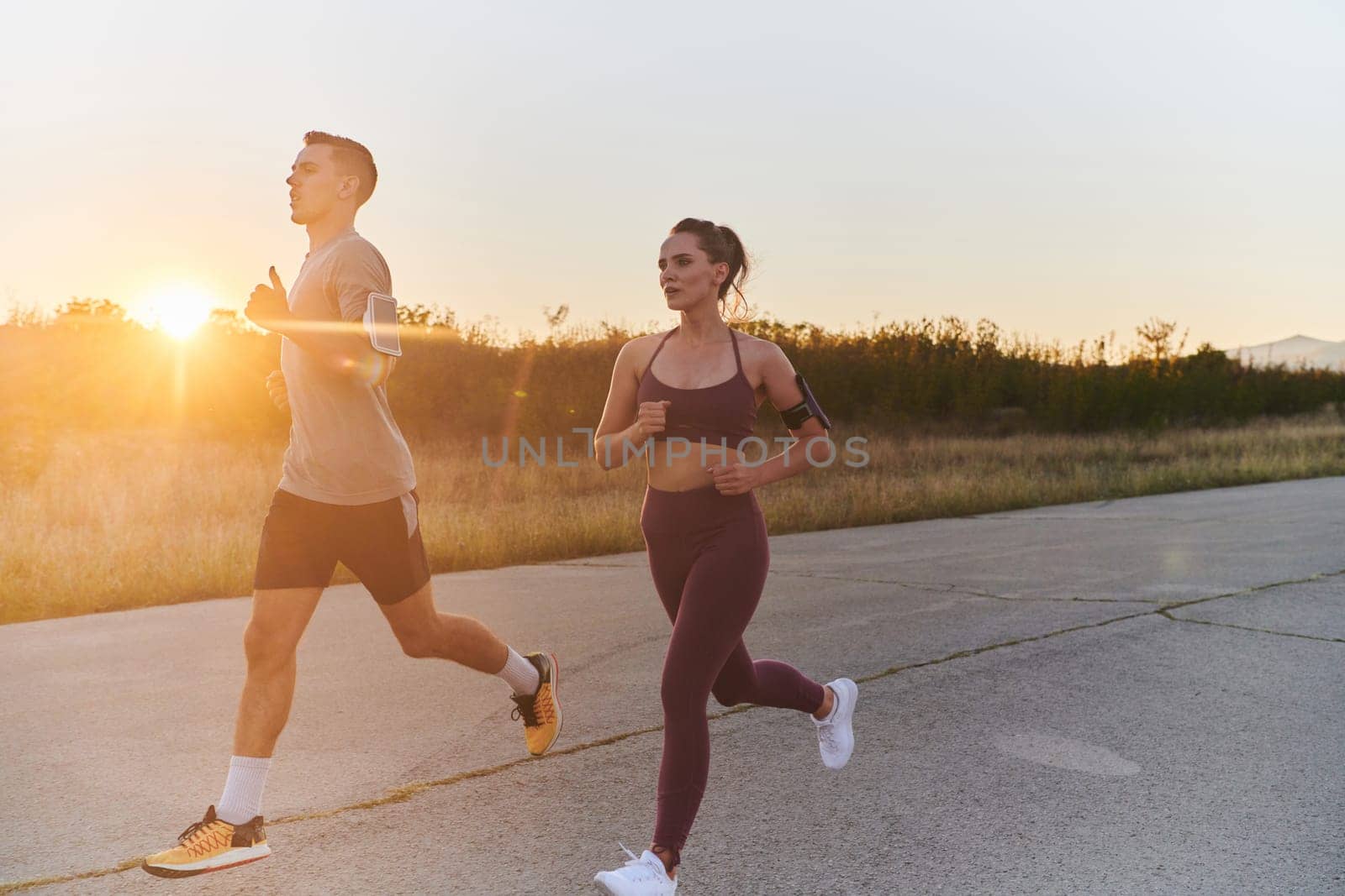 A handsome young couple running together during the early morning hours, with the mesmerizing sunrise casting a warm glow, symbolizing their shared love and vitality.