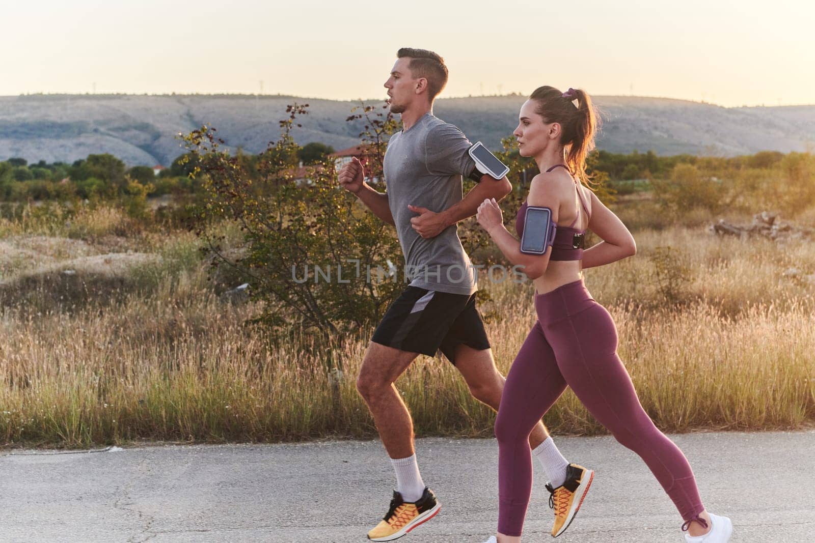 A handsome young couple running together during the early morning hours, with the mesmerizing sunrise casting a warm glow, symbolizing their shared love and vitality.