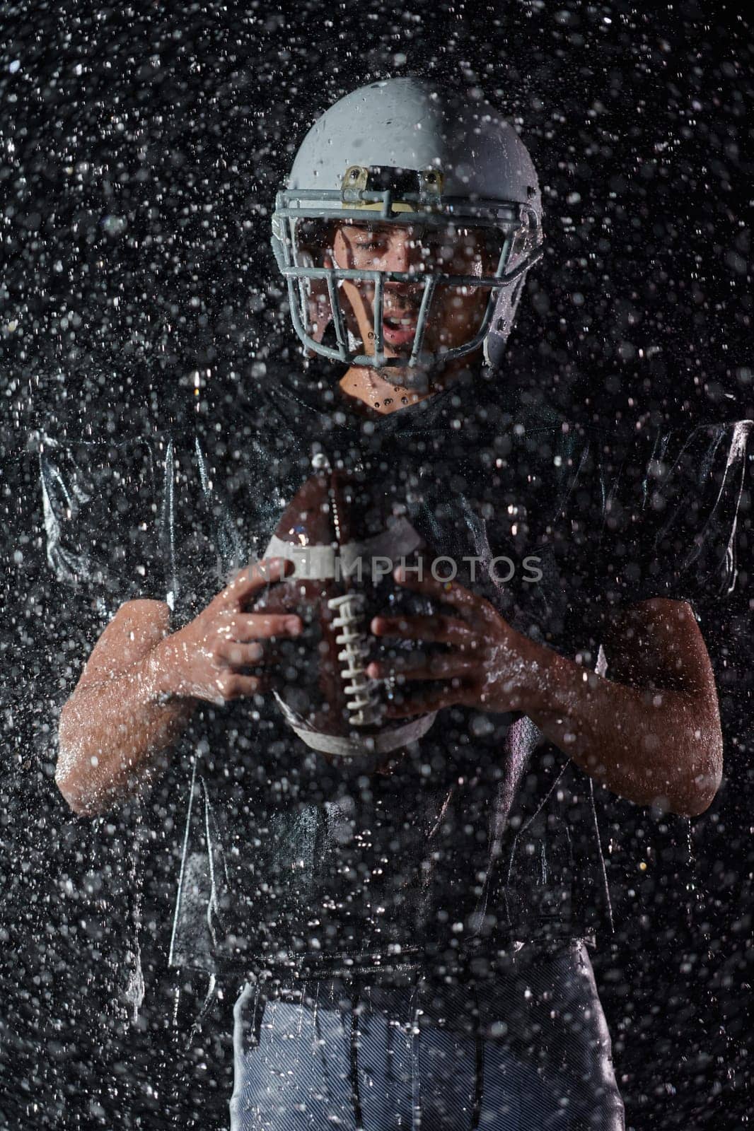 American Football Field: Lonely Athlete Warrior Standing on a Field Holds his Helmet and Ready to Play. Player Preparing to Run, Attack and Score Touchdown. Rainy Night with Dramatic Fog, Blue Light by dotshock