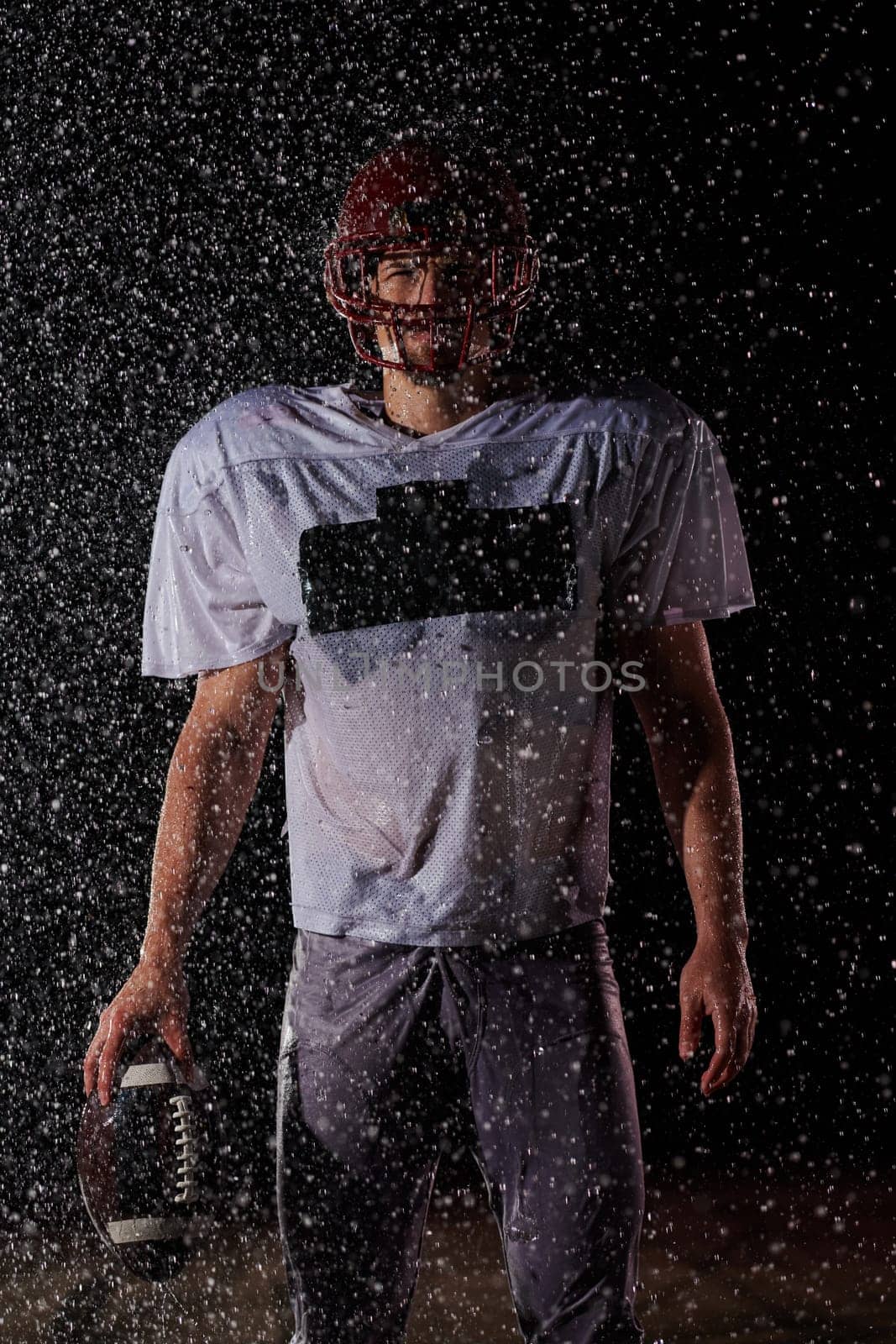 American Football Field: Lonely Athlete Warrior Standing on a Field Holds his Helmet and Ready to Play. Player Preparing to Run, Attack and Score Touchdown. Rainy Night with Dramatic Fog, Blue Light.