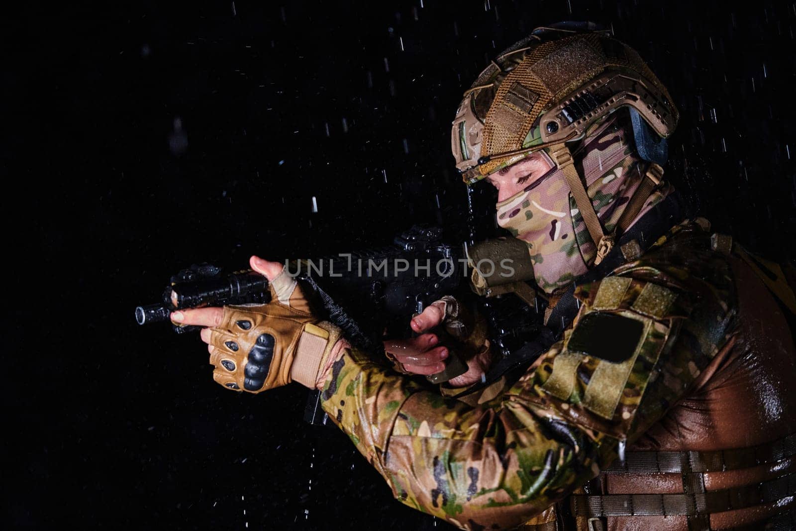 Army soldier in Combat Uniforms with an assault rifle, plate carrier and combat helmet going on a dangerous mission on a rainy night