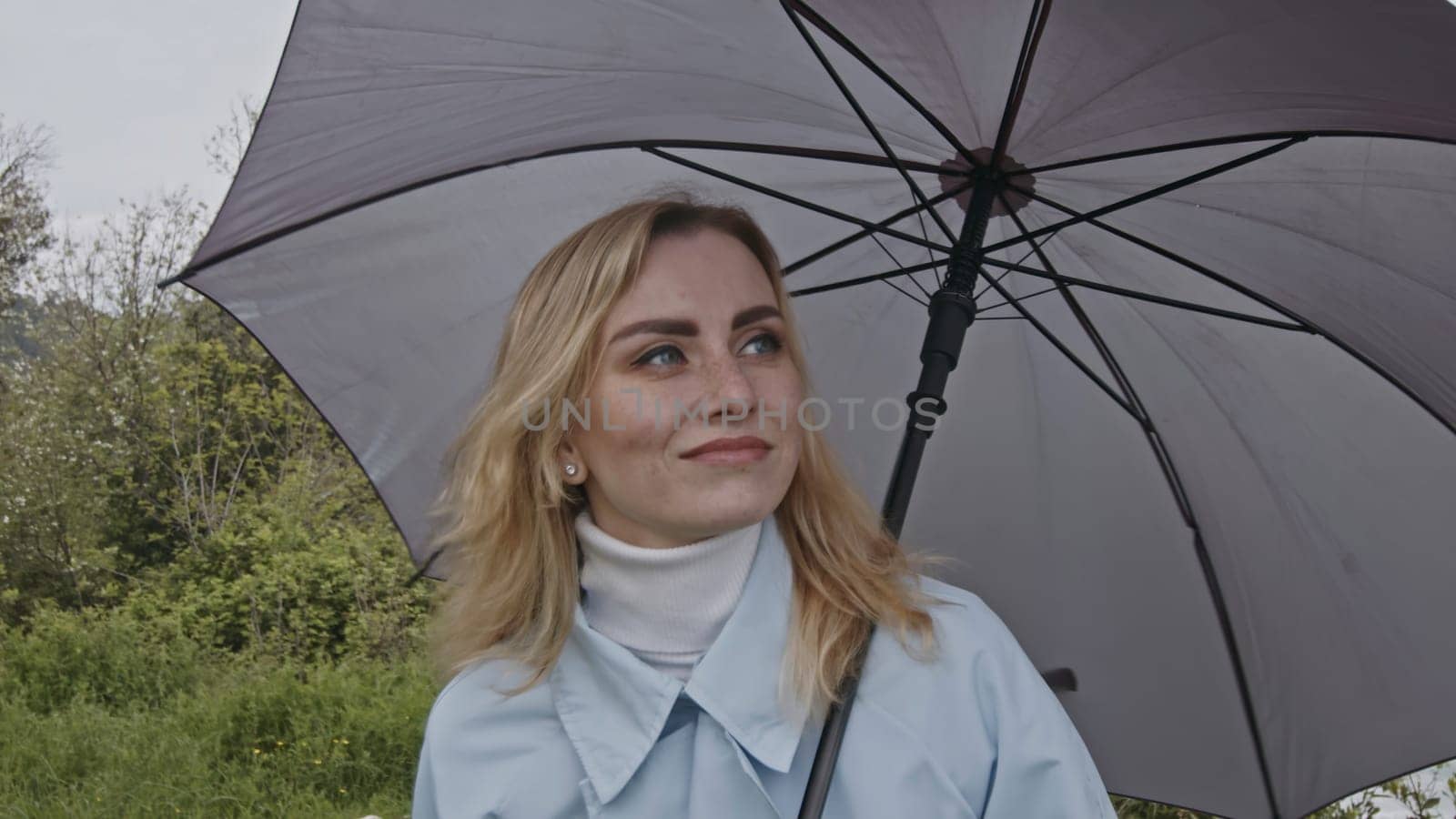 Portrait of cute romantic blonde woman smiling in green spring park. Stock clip. Young woman with grey umbrella. by Mediawhalestock