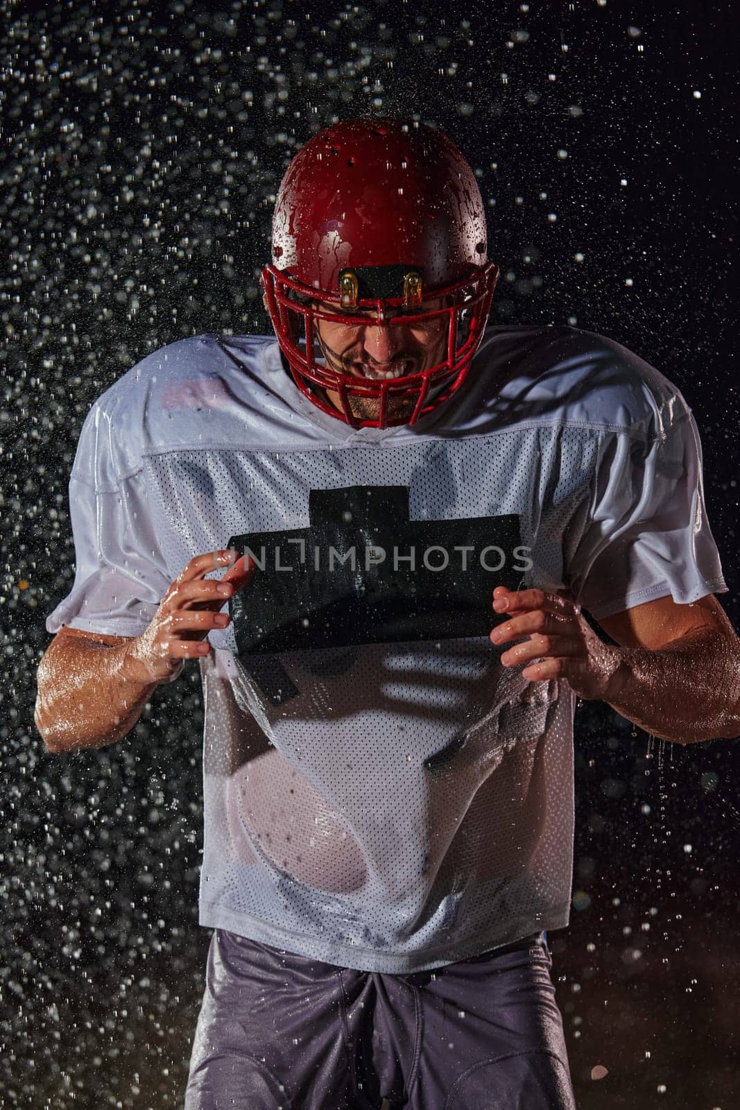 American Football Field: Lonely Athlete Warrior Standing on a Field Holds his Helmet and Ready to Play. Player Preparing to Run, Attack and Score Touchdown. Rainy Night with Dramatic Fog, Blue Light.