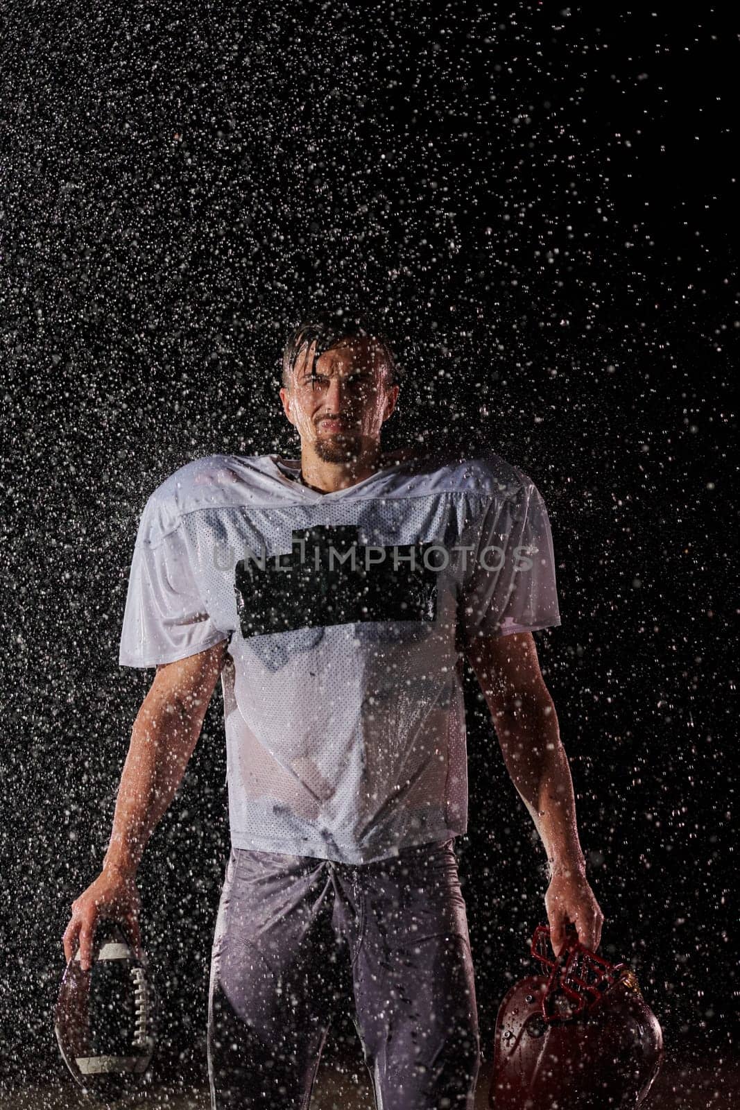 American Football Field: Lonely Athlete Warrior Standing on a Field Holds his Helmet and Ready to Play. Player Preparing to Run, Attack and Score Touchdown. Rainy Night with Dramatic Fog, Blue Light.