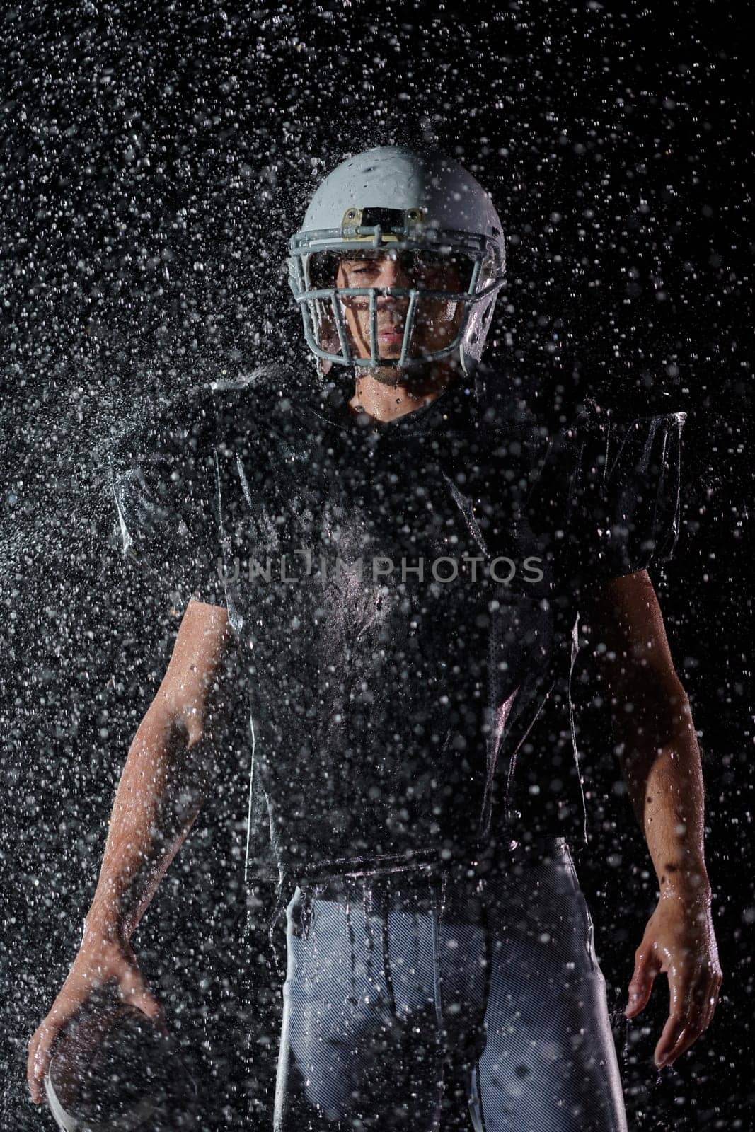 American Football Field: Lonely Athlete Warrior Standing on a Field Holds his Helmet and Ready to Play. Player Preparing to Run, Attack and Score Touchdown. Rainy Night with Dramatic Fog, Blue Light.