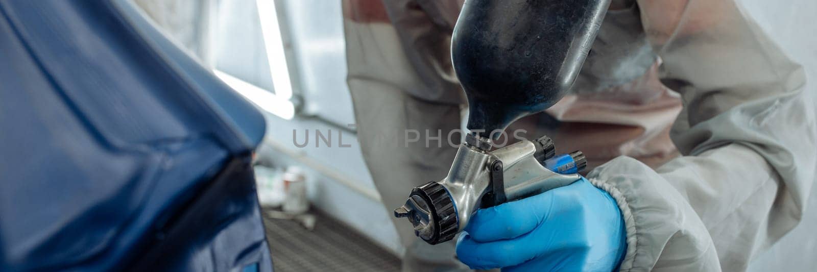 Banner . automobile repairman painter hand in protective glove with airbrush pulverizer painting car body in paint chamber