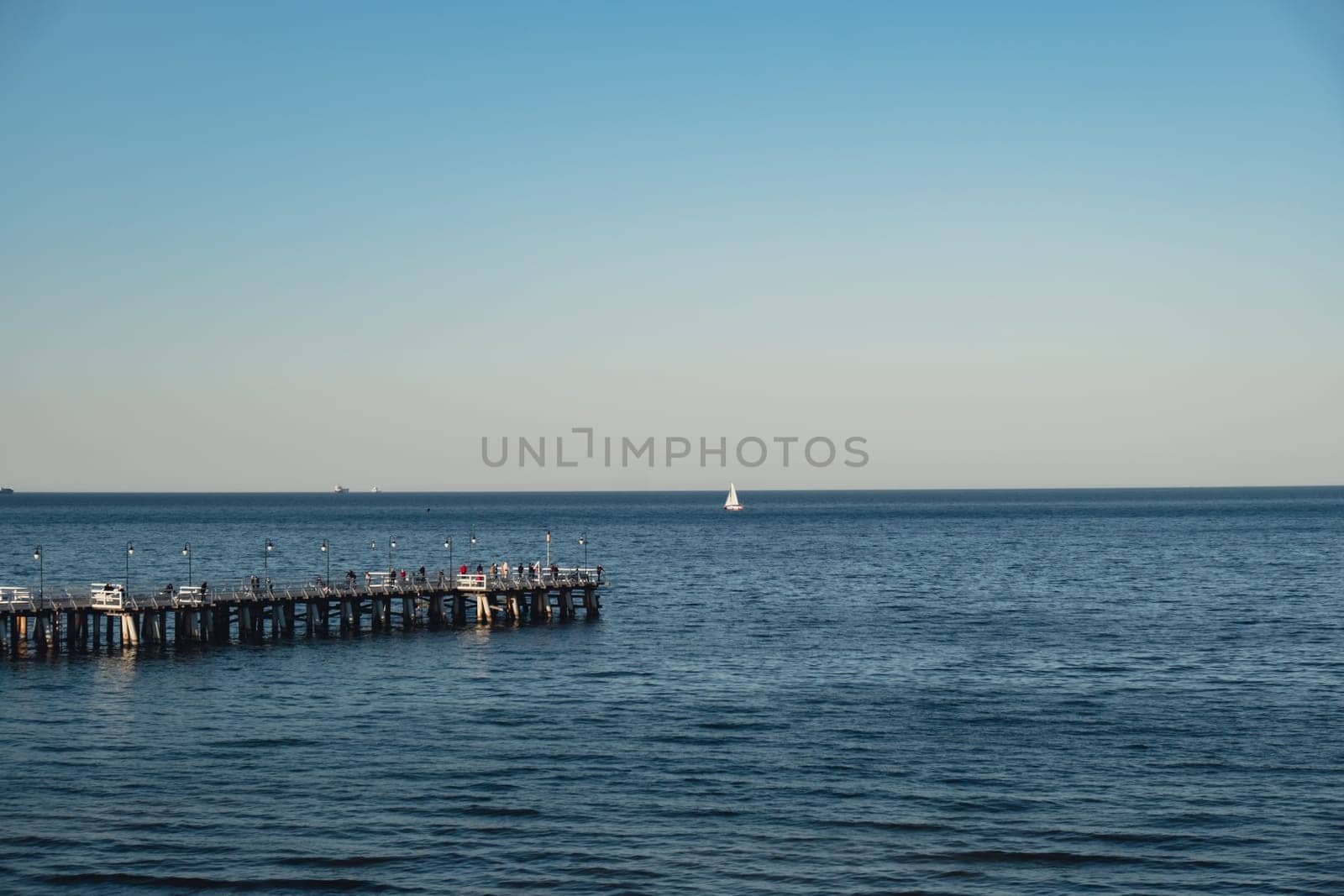 Storm sea waves empty wooden pier in dramatic blue sky background. Seascape with running splashing sea waves. Sandy beach vacation getaway in Gdansk Poland. Copy space for your text