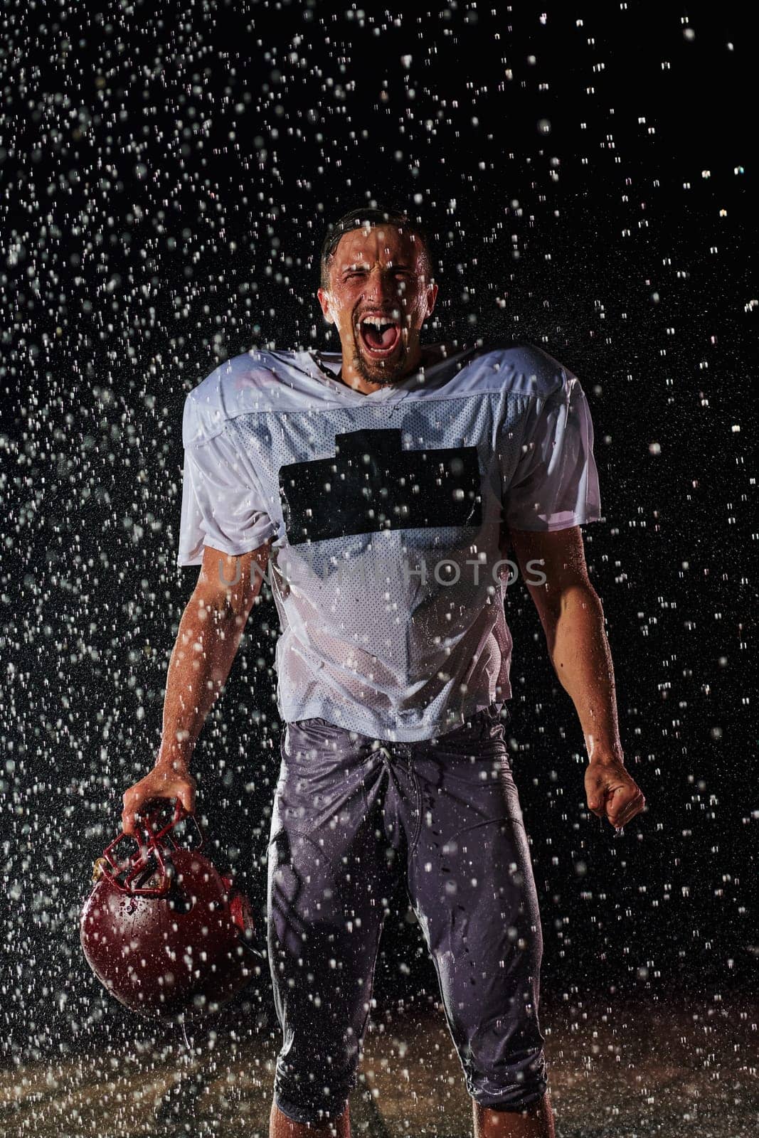 American Football Field: Lonely Athlete Warrior Standing on a Field Holds his Helmet and Ready to Play. Player Preparing to Run, Attack and Score Touchdown. Rainy Night with Dramatic Fog, Blue Light.