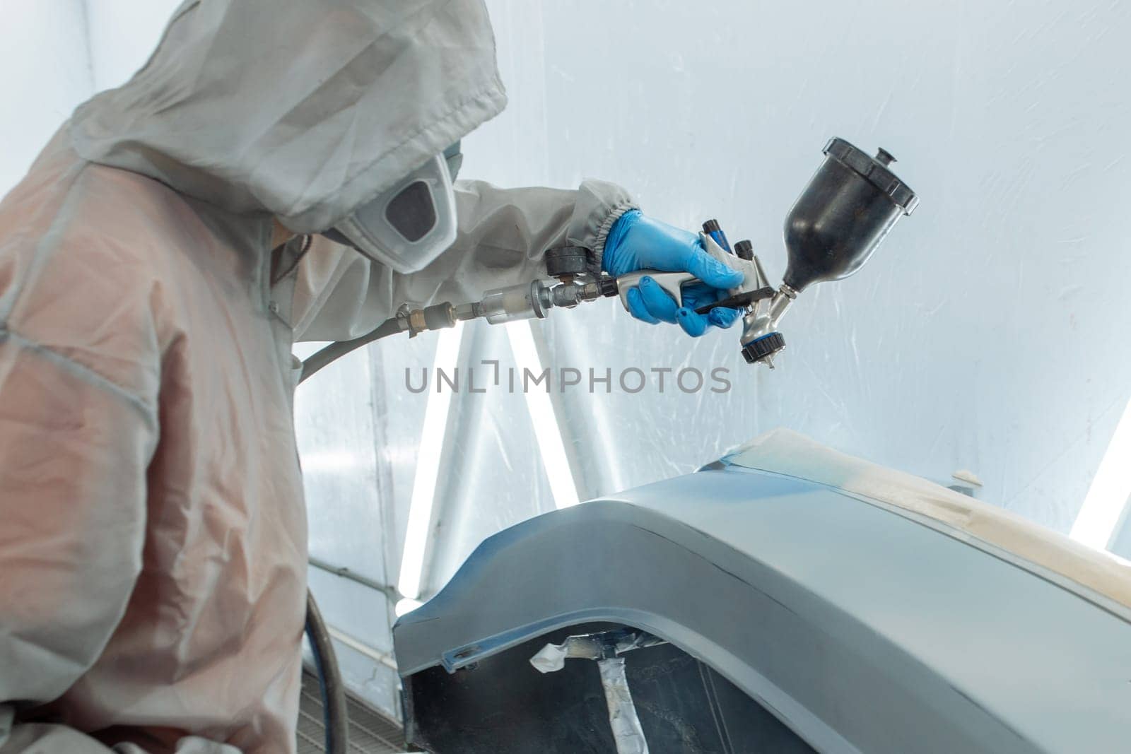 automobile repairman painter hand in protective glove with airbrush pulverizer painting car body in paint chamber