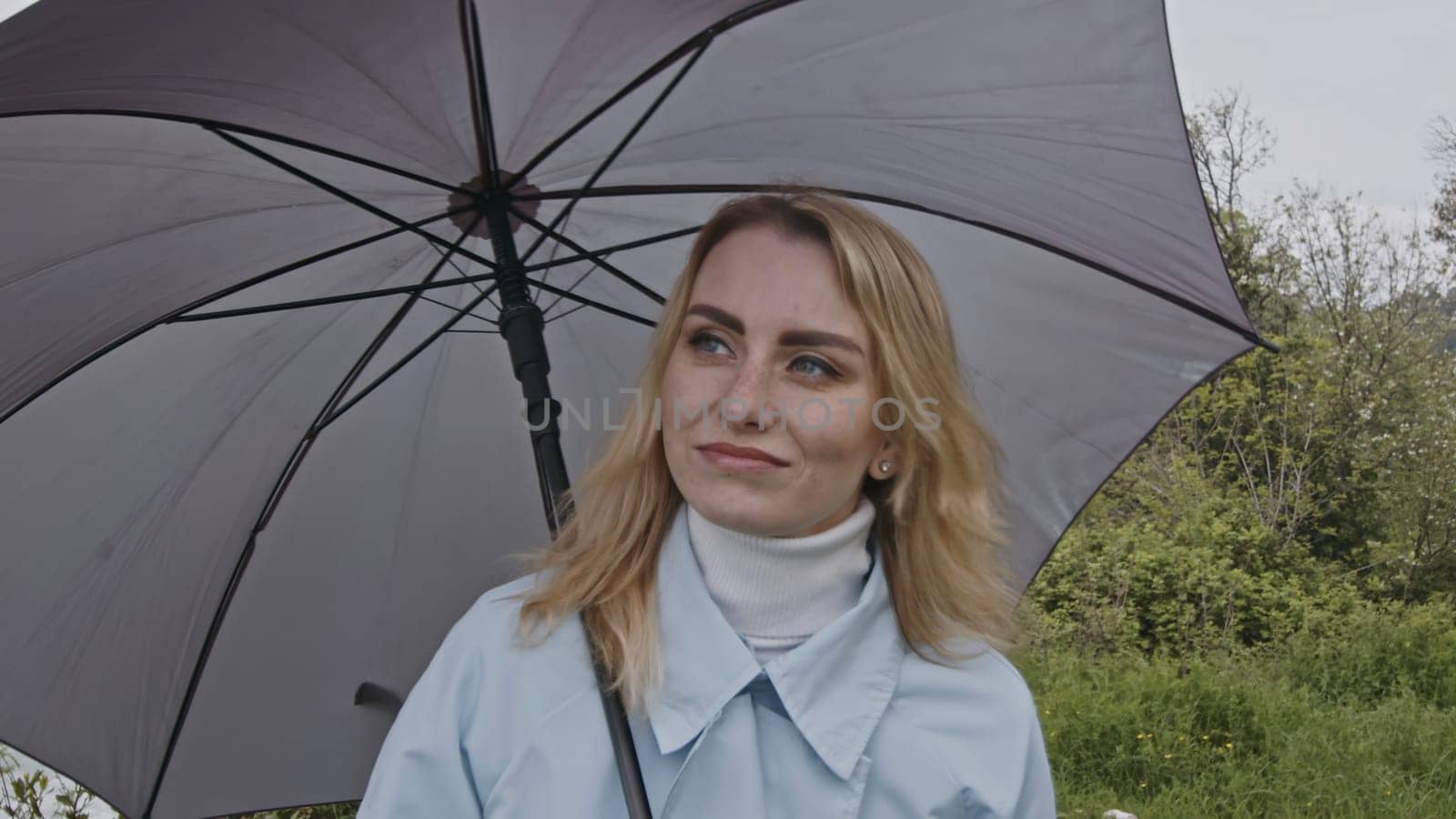 Portrait of cute romantic blonde woman smiling in green spring park. Stock clip. Young woman with grey umbrella. by Mediawhalestock