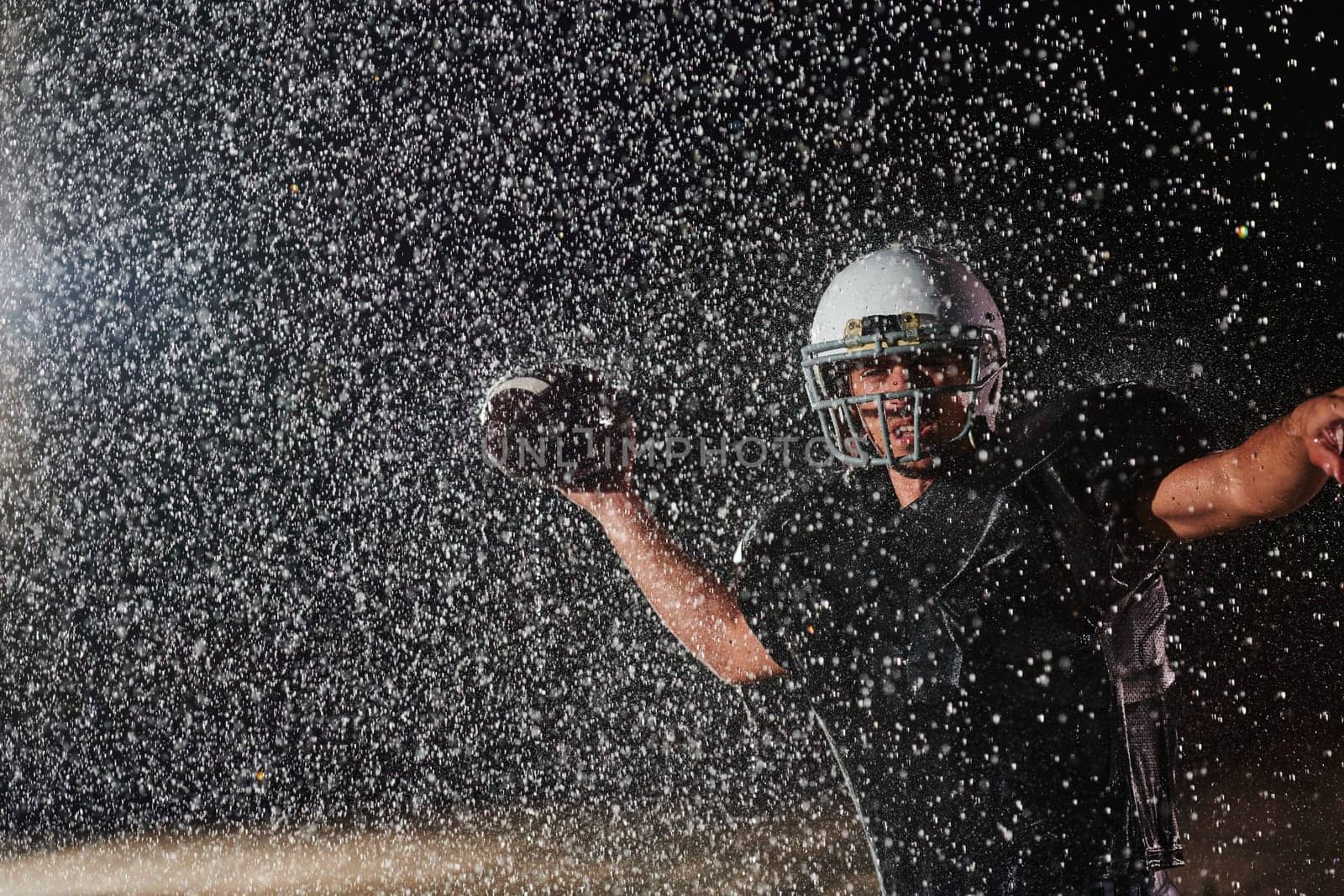 American Football Field: Lonely Athlete Warrior Standing on a Field Holds his Helmet and Ready to Play. Player Preparing to Run, Attack and Score Touchdown. Rainy Night with Dramatic Fog, Blue Light by dotshock