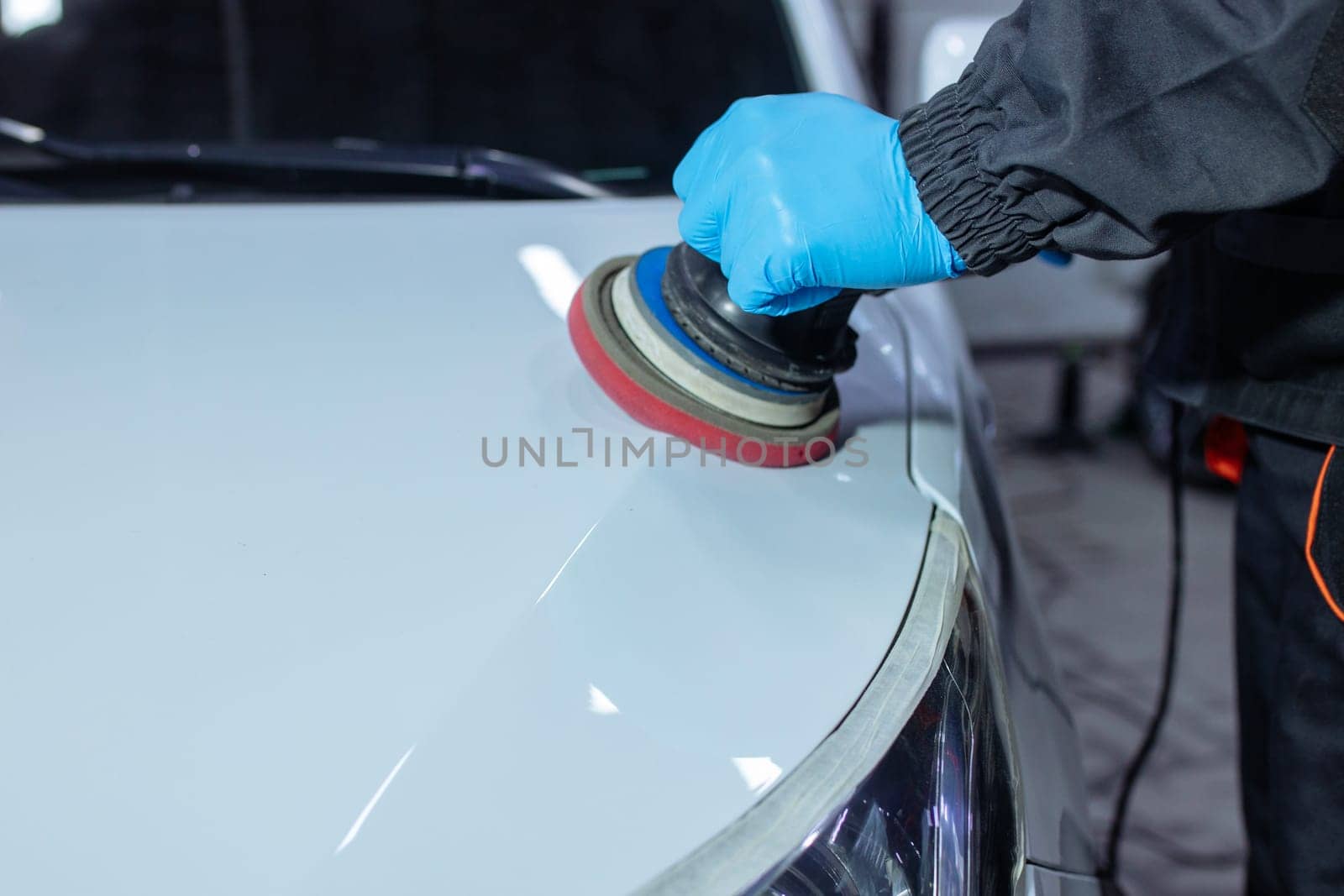 Serviceman polishing car body with machine in a workshop