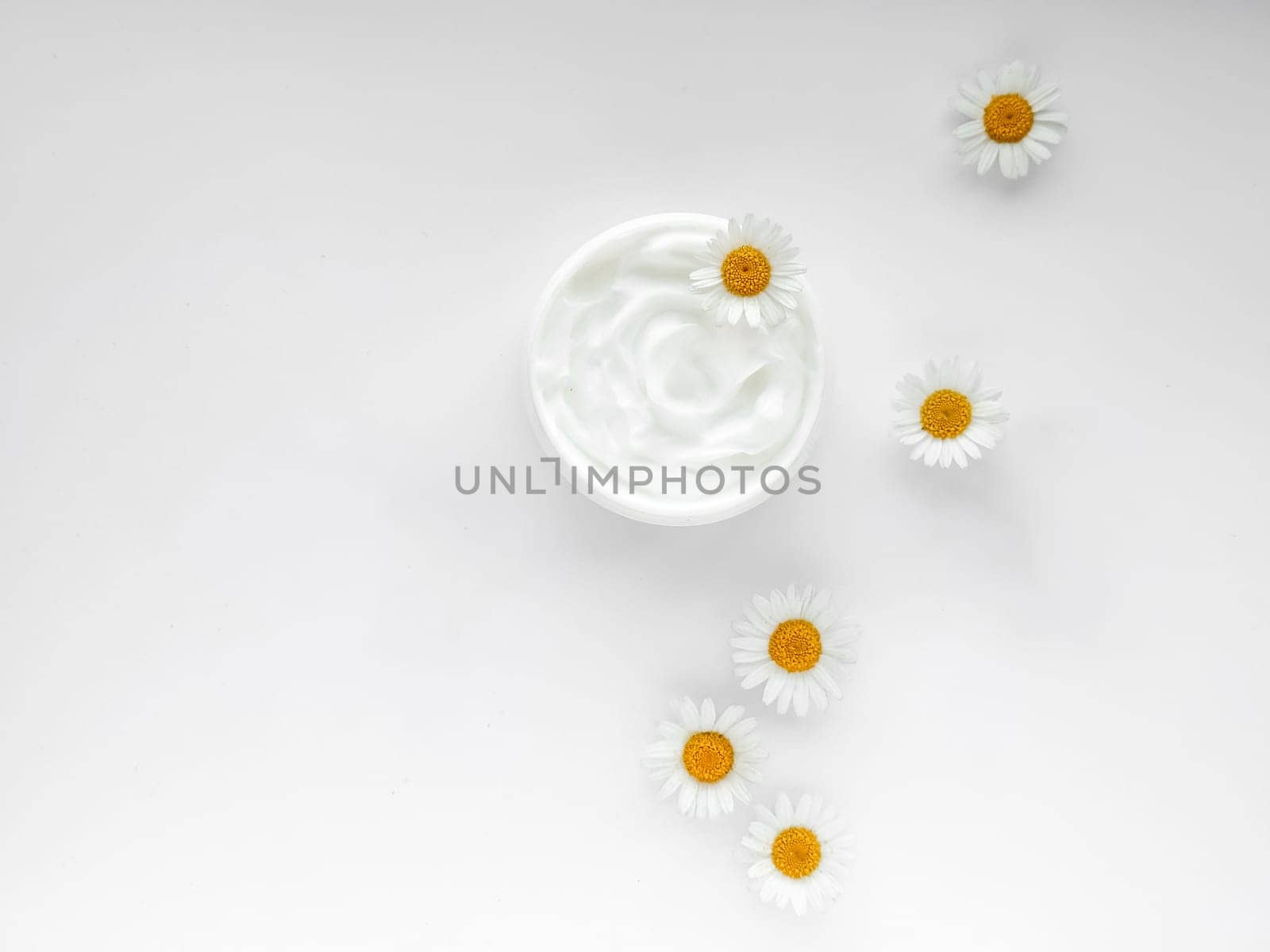 Open jar of white hand or body cream with chamomile flowers on white background. Top view composition with copy space. For skincare and beauty product concept. High quality photo