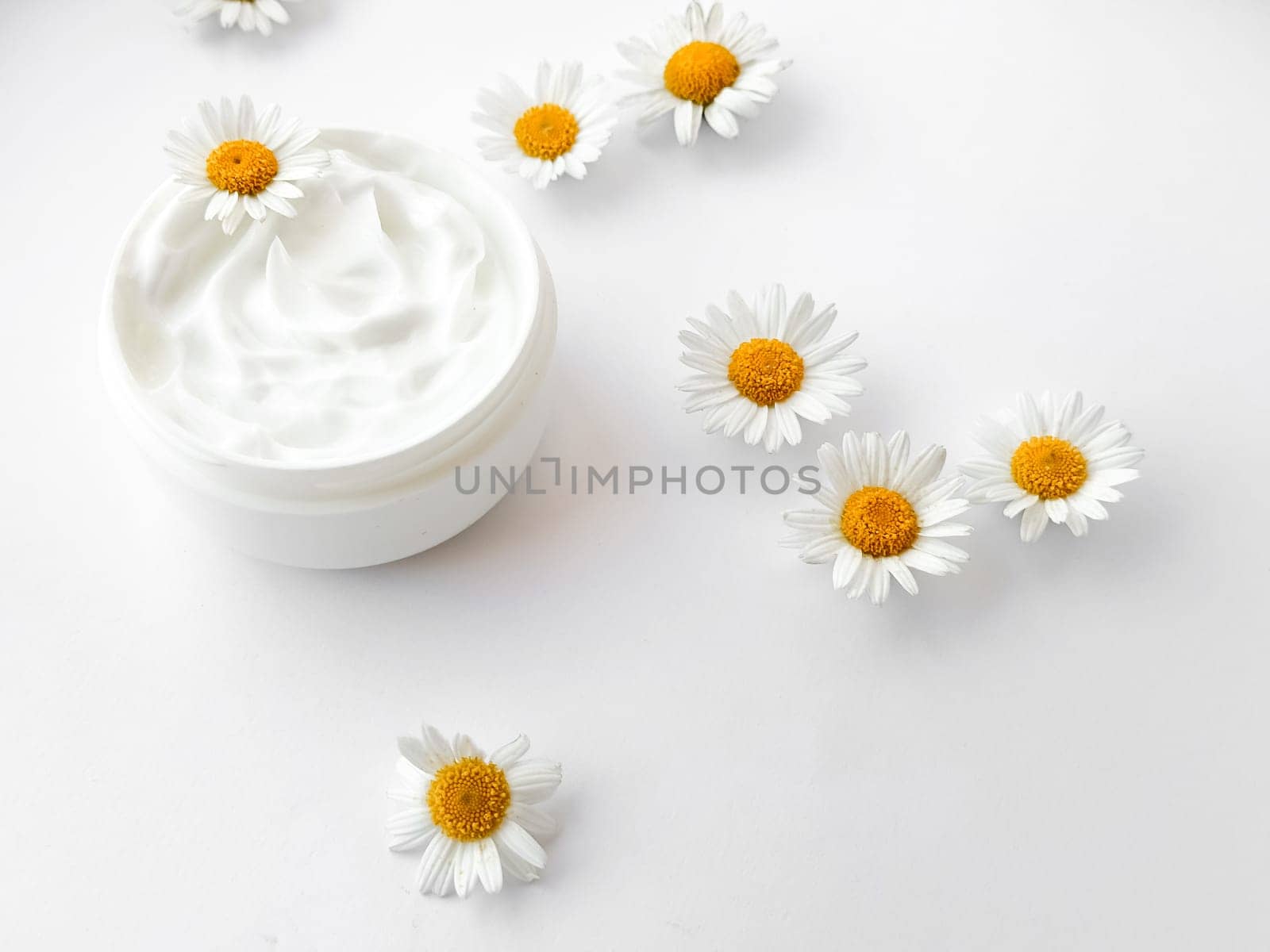 Open jar of white hand or body cream with chamomile flowers on white background. Flat lay composition. For skincare and beauty product concept. High quality photo