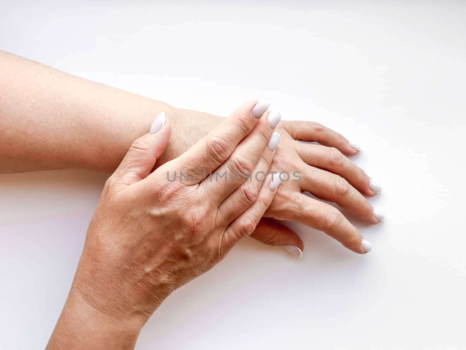 Hands middle age woman with white manicured nails gently touching each other on white background, top view. Flat lay composition. Skincare and hand care or mother love concept. High quality photo