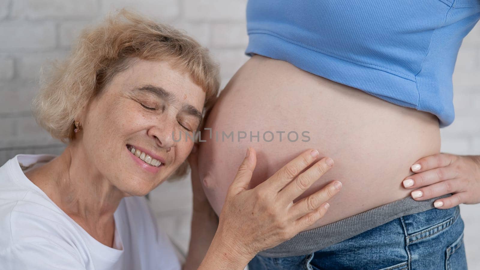 An elderly woman leans against the belly of her pregnant daughter. Close-up