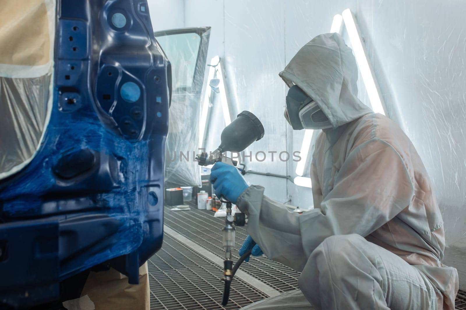 automobile repairman painter hand in protective glove with airbrush pulverizer painting car body in paint chamber