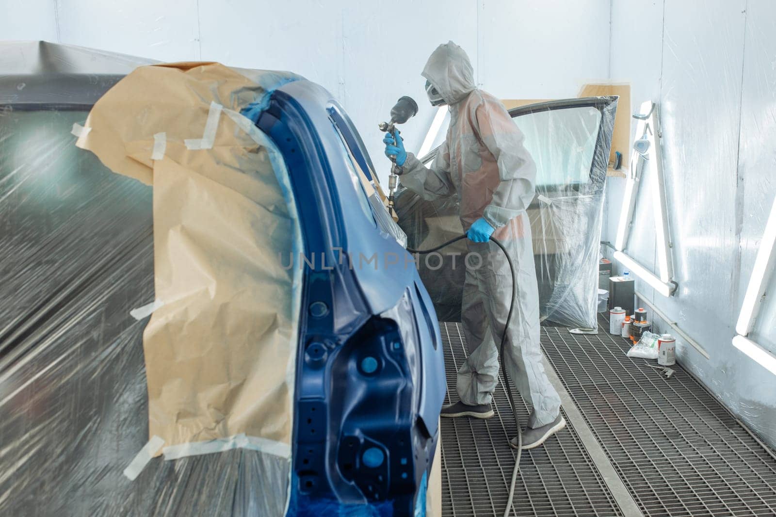 automobile repairman painter hand in protective glove with airbrush pulverizer painting car body in paint chamber