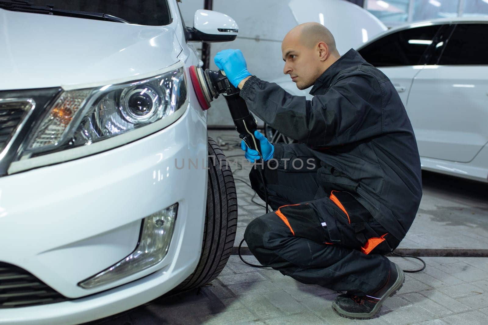 Serviceman polishing car body with machine in a workshop