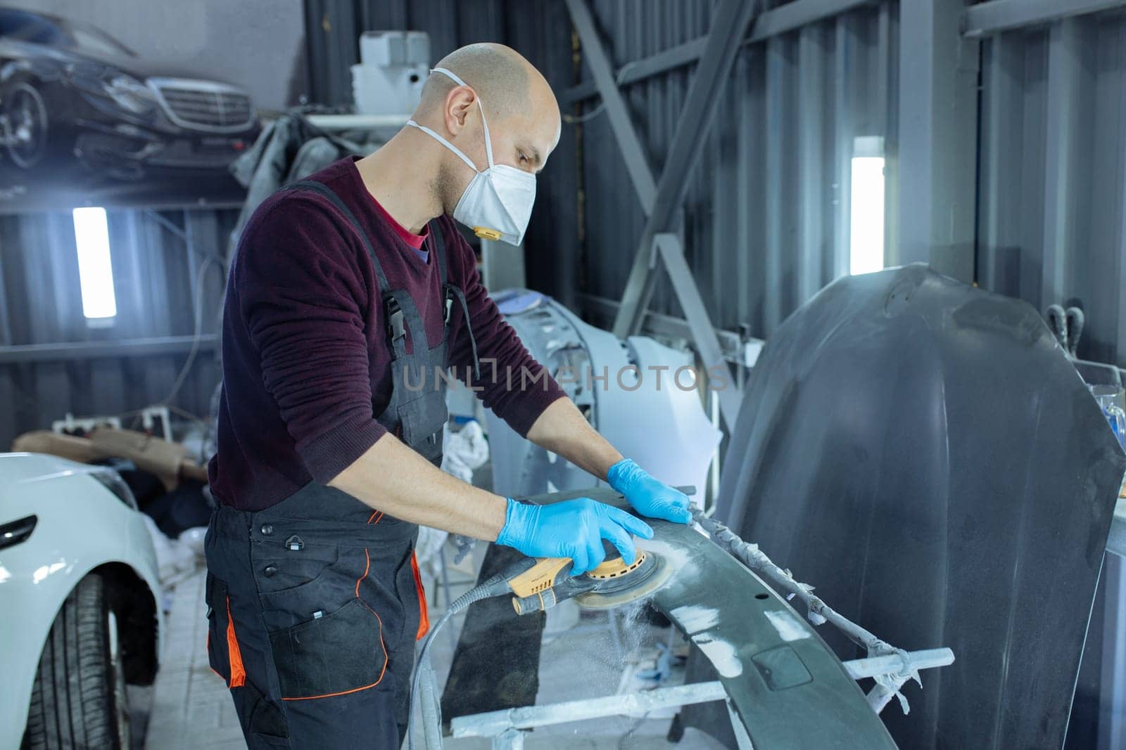 Sanding a car body part with electrical grinder machine before painting, vehicle body repair service