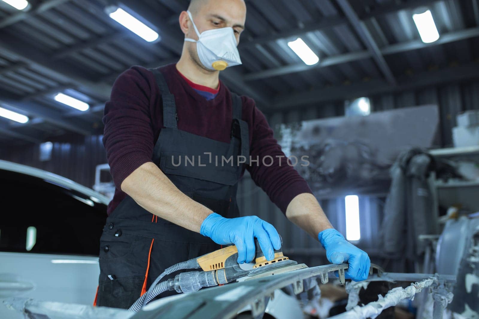 Sanding a car body part with electrical grinder machine before painting, vehicle body repair service