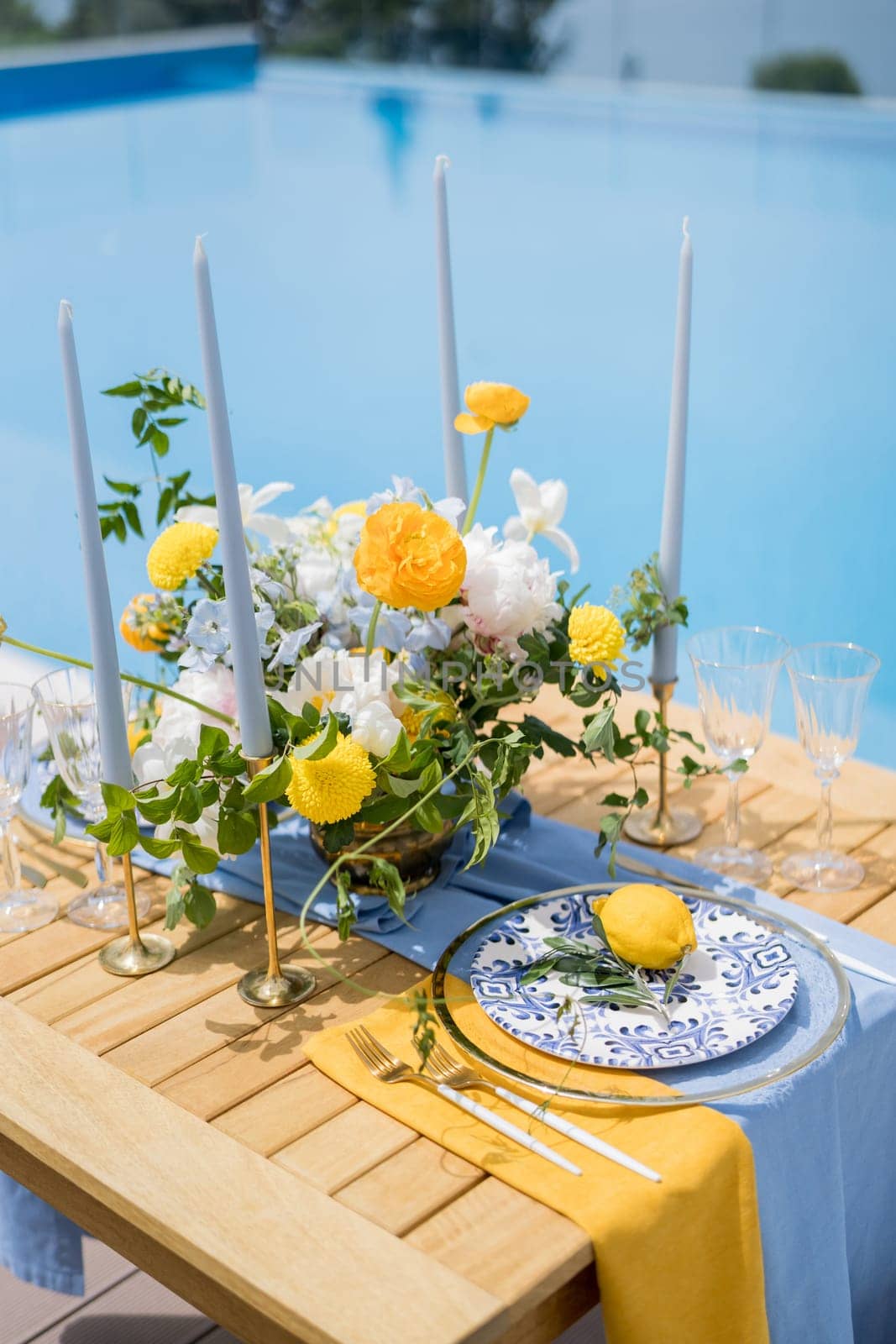 Lemon lies on a plate near a bouquet of flowers on a festive table by the pool. High quality photo