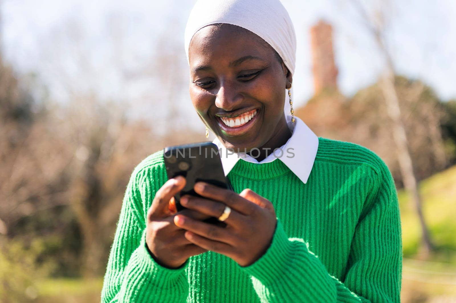 young african woman smiling happy using mobile phone outdoors, concept of technology of communication and modern lifestyle