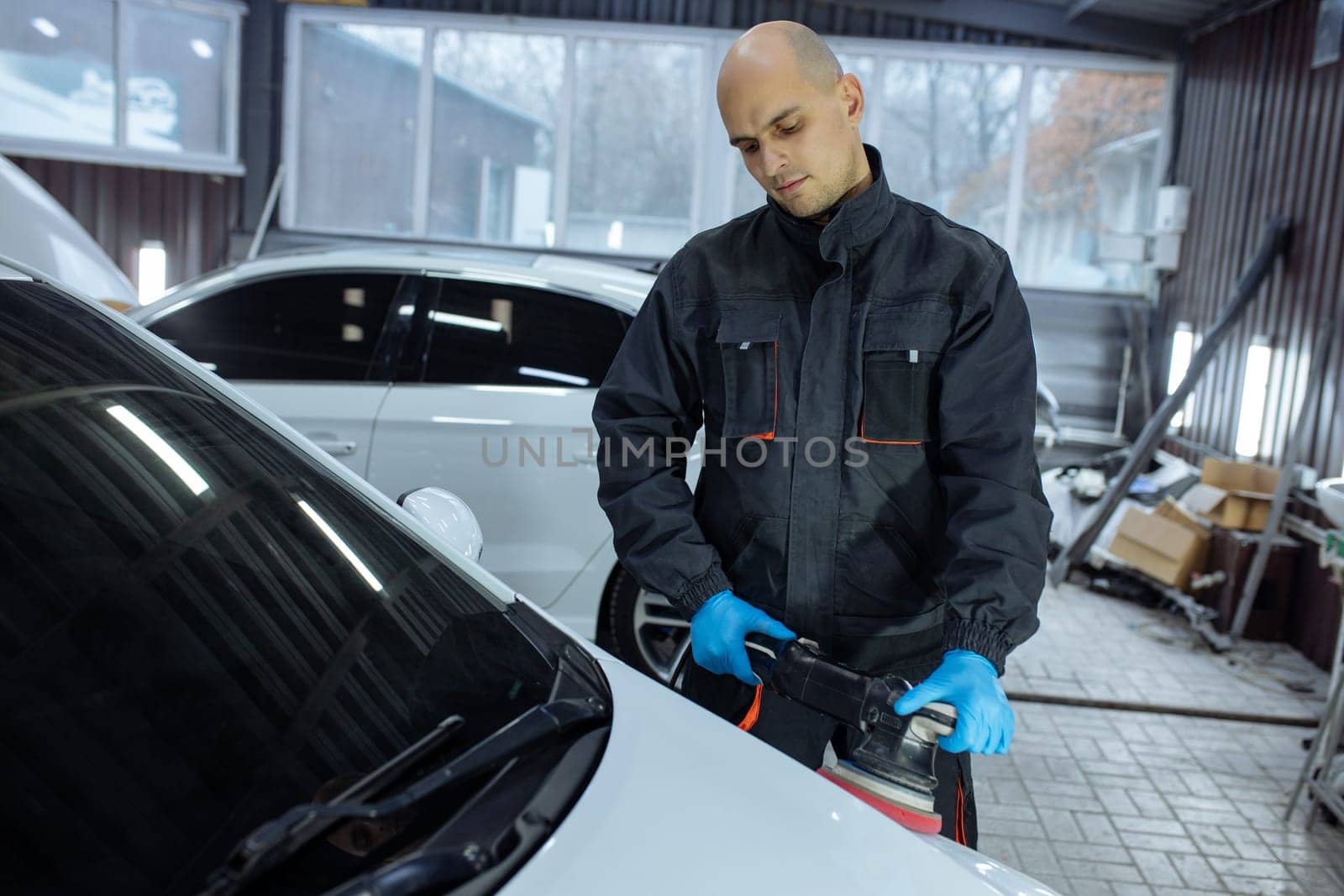 Serviceman polishing car body with machine in a workshop