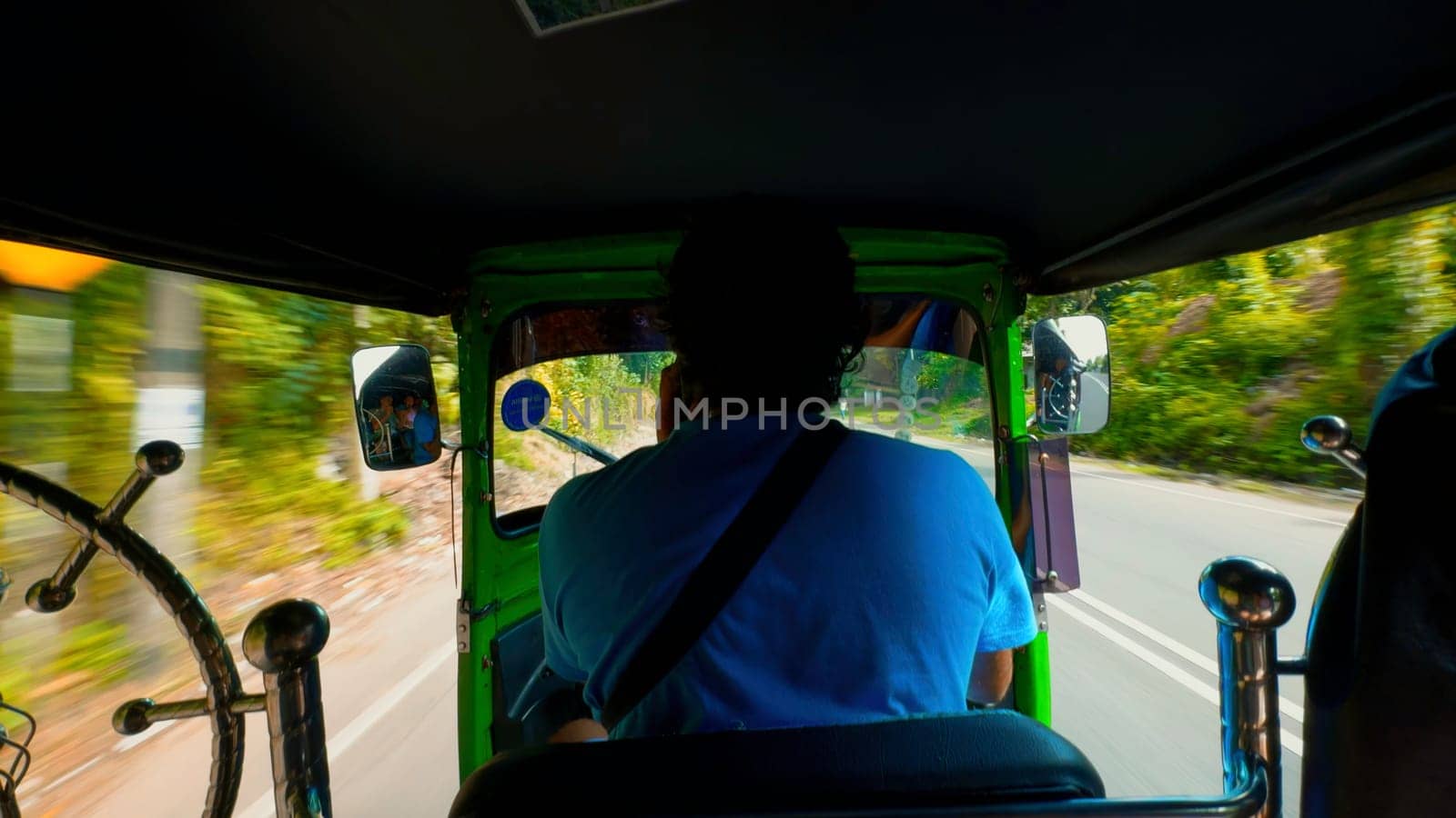Rear view of a tuk-tuk or motorcycle driver carrying passengers along green trees and cars. Action. Concept of travelling. by Mediawhalestock