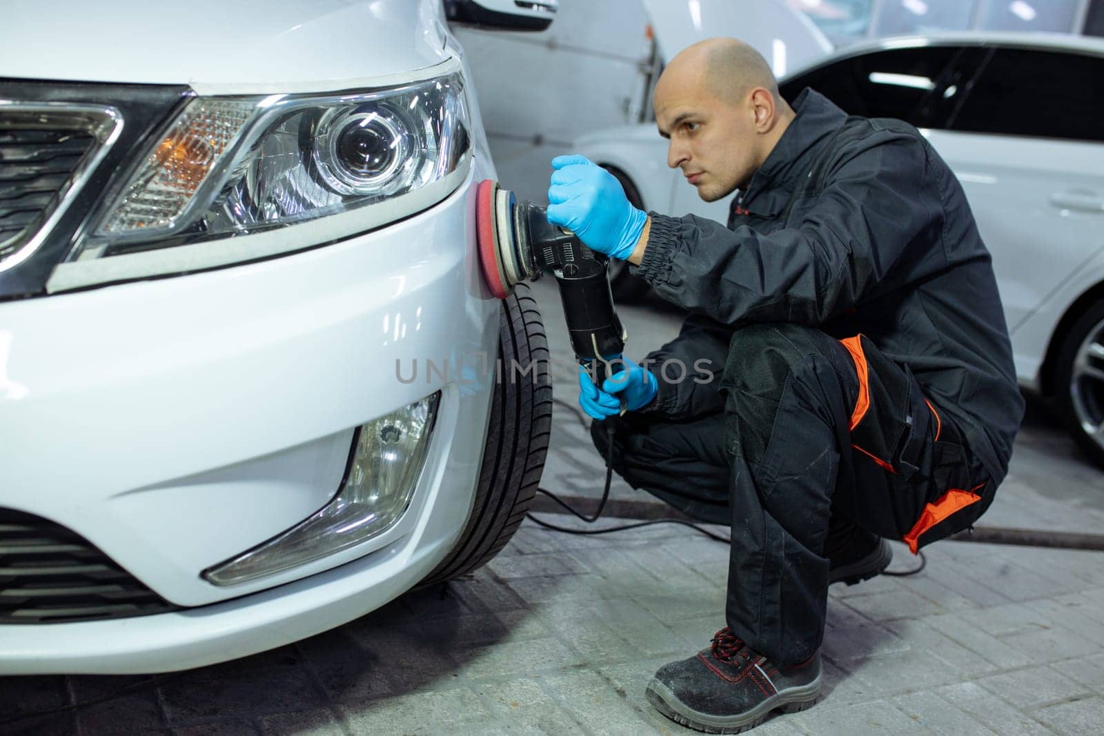 Serviceman polishing car body with machine in a workshop