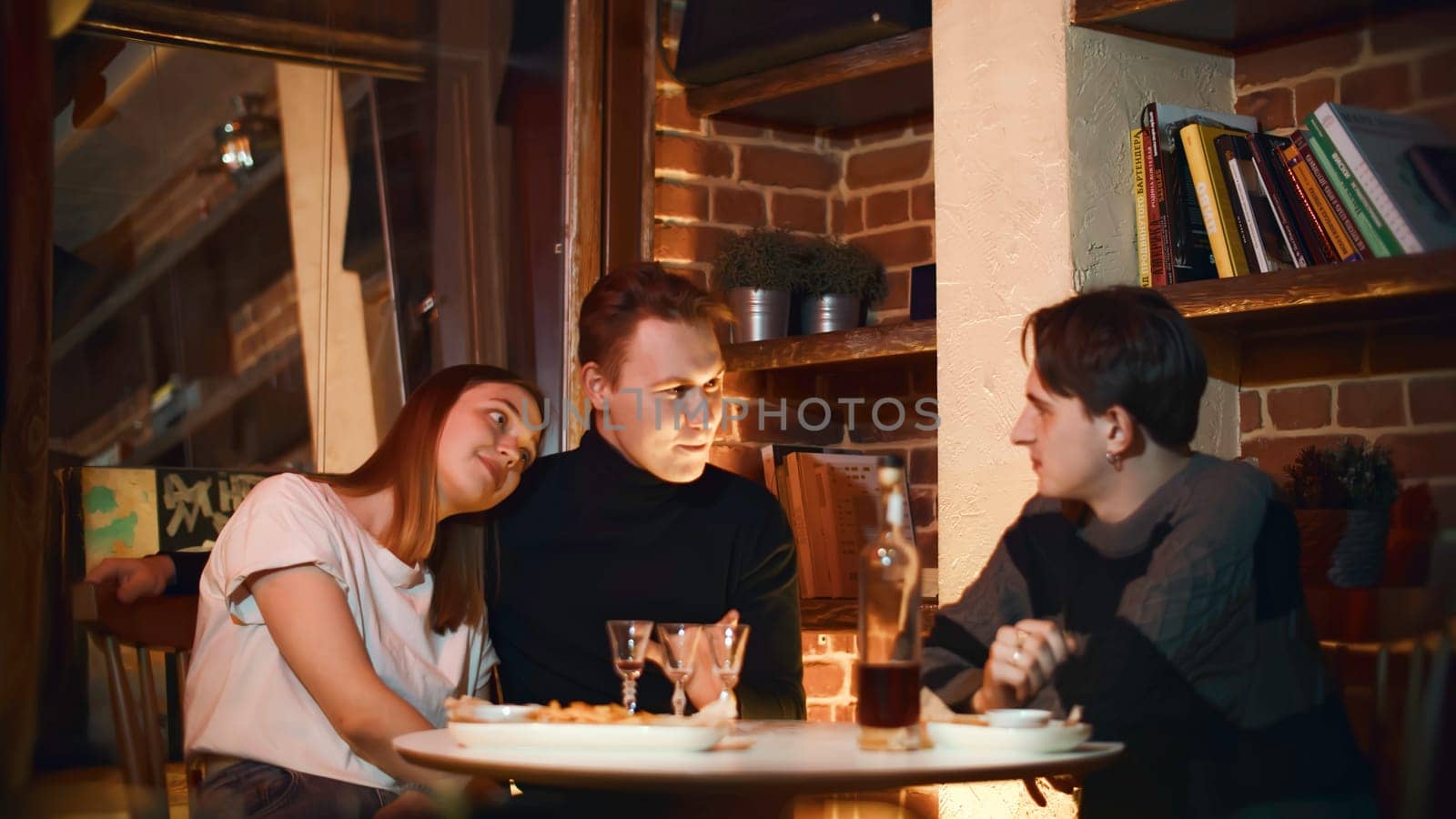 Girl with boyfriend and friend in restaurant. Media. Friends chat in cozy bar with alcoholic drink. Friends have drink in cozy bar on weekend evening.