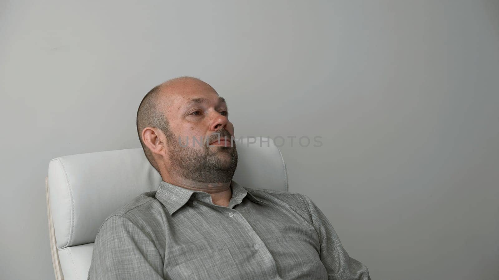Frustrated man in shirt during therapy session in psychologist office. Silent bald middle age man portrait in armchair